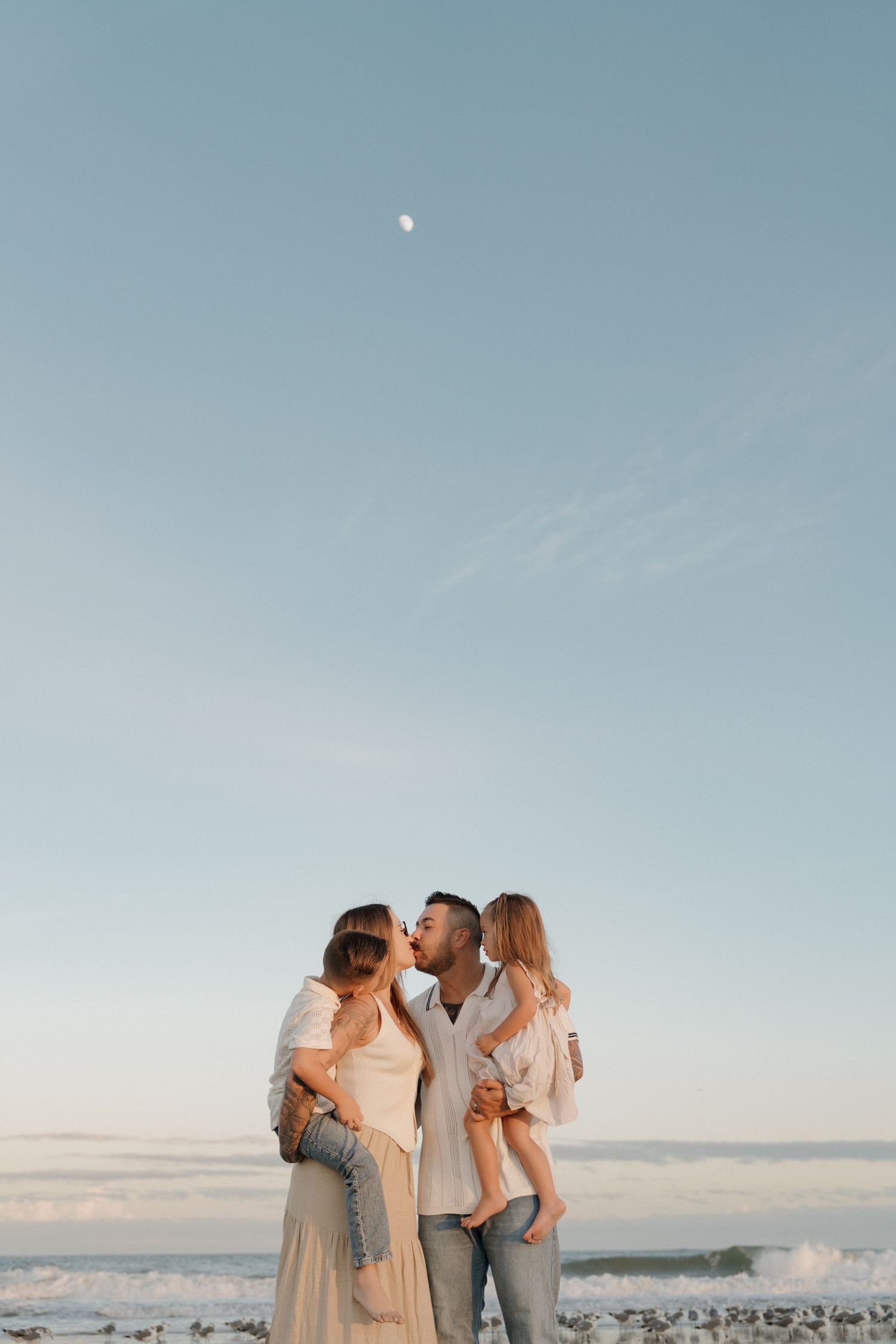 A family shares an intimate moment against a dusky sky with a faint moon visible above.