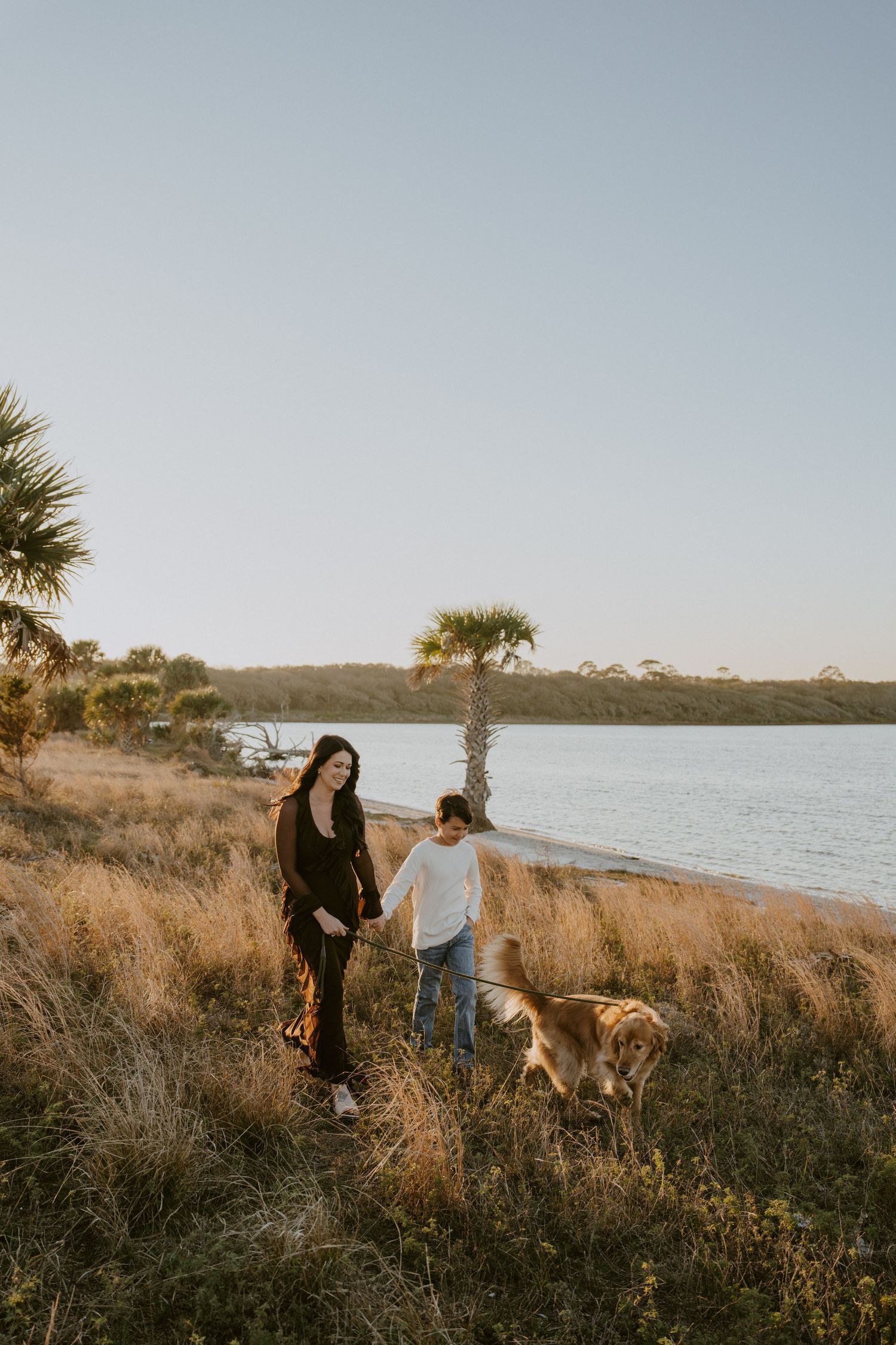 Coastal walking trail scene with people and a dog enjoying the ocean view at golden hour.