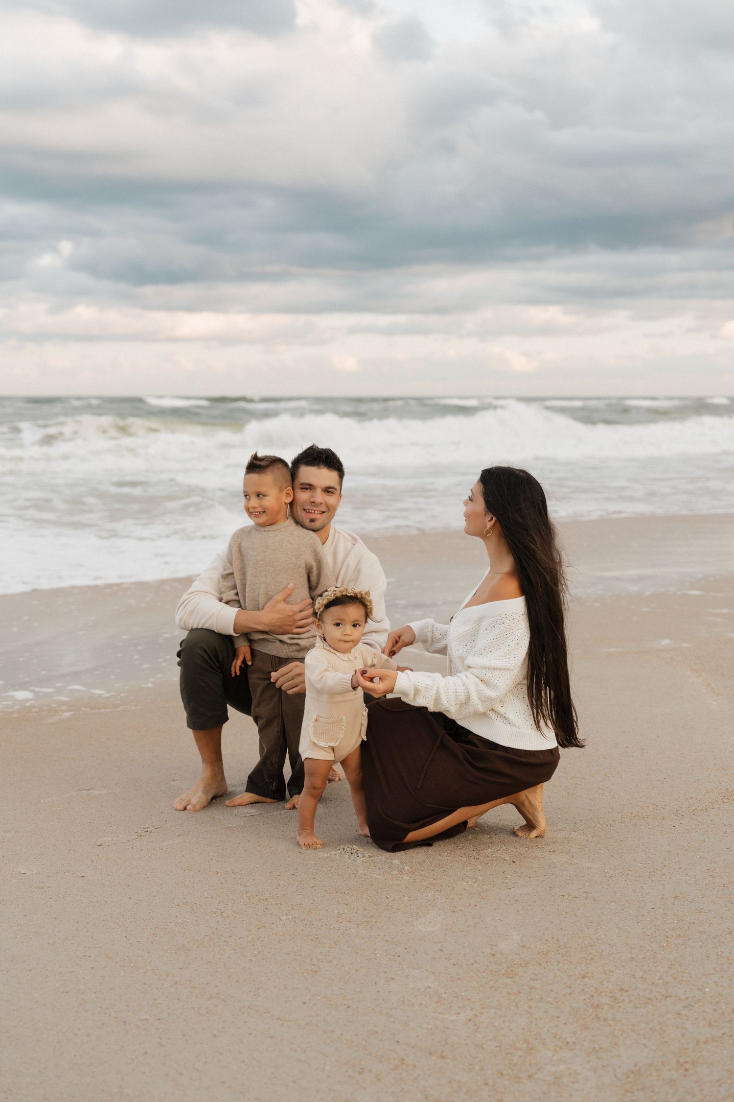 Family sitting together on a cloudy beach with waves crashing in the background.