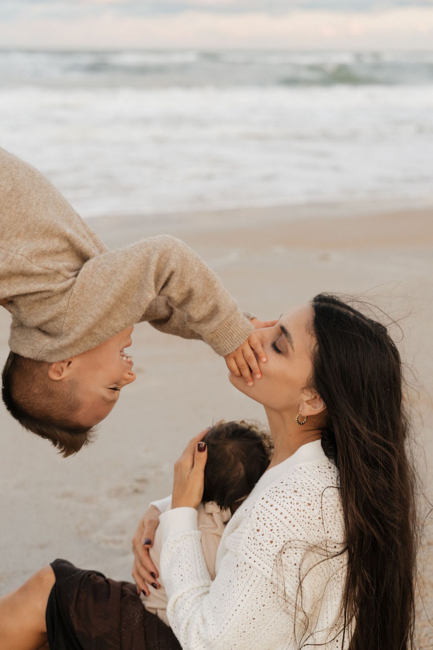 A loving family shares an intimate moment together on a cloudy beach at sunset.