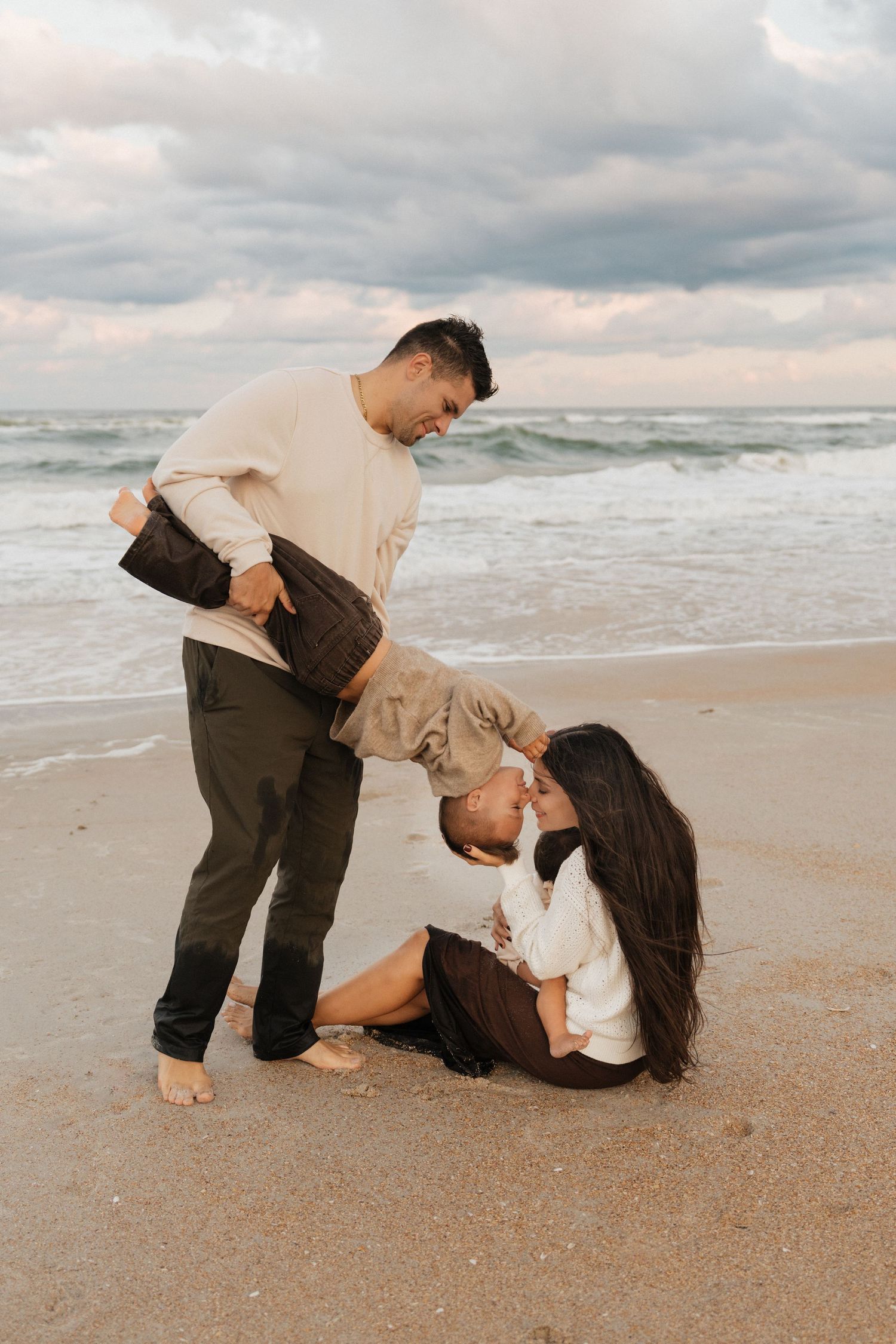 Couple shares playful romantic moments on a sandy beach at sunset with waves in the background.