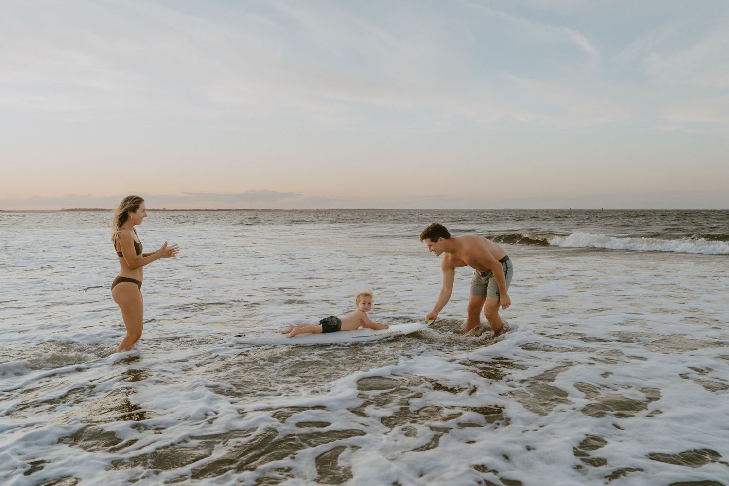 A family plays together in the ocean waves at sunset on a sandy beach.