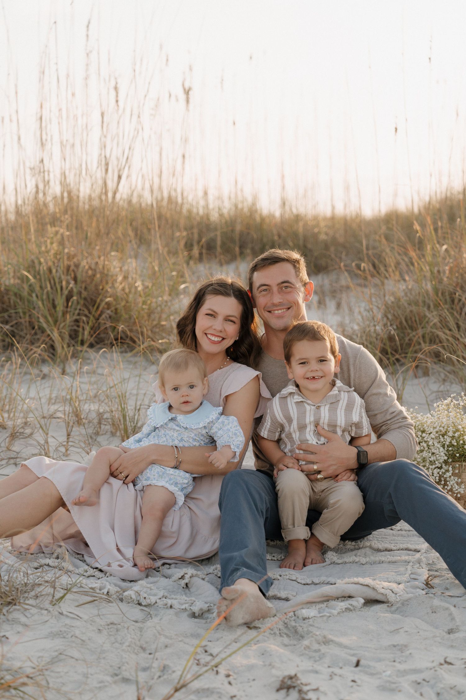 Family beach portrait at sunset with sand dunes and sea grass creating a natural backdrop.