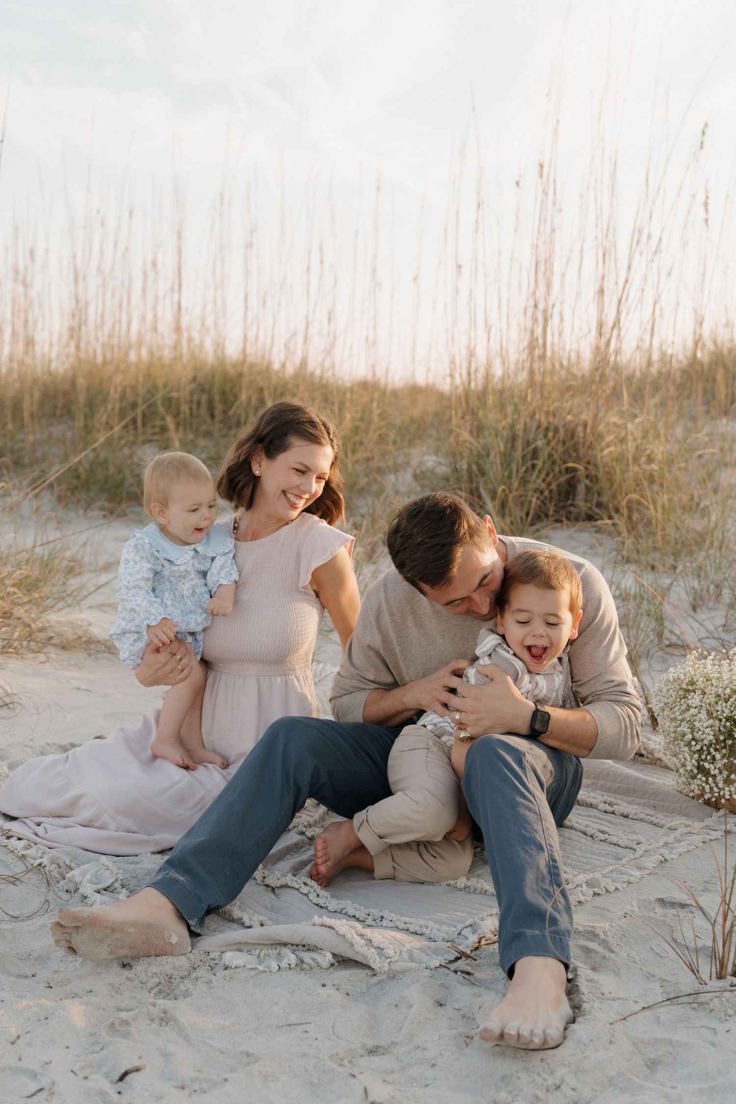 A family shares intimate moments while sitting together on sandy beach dunes during a photo session.