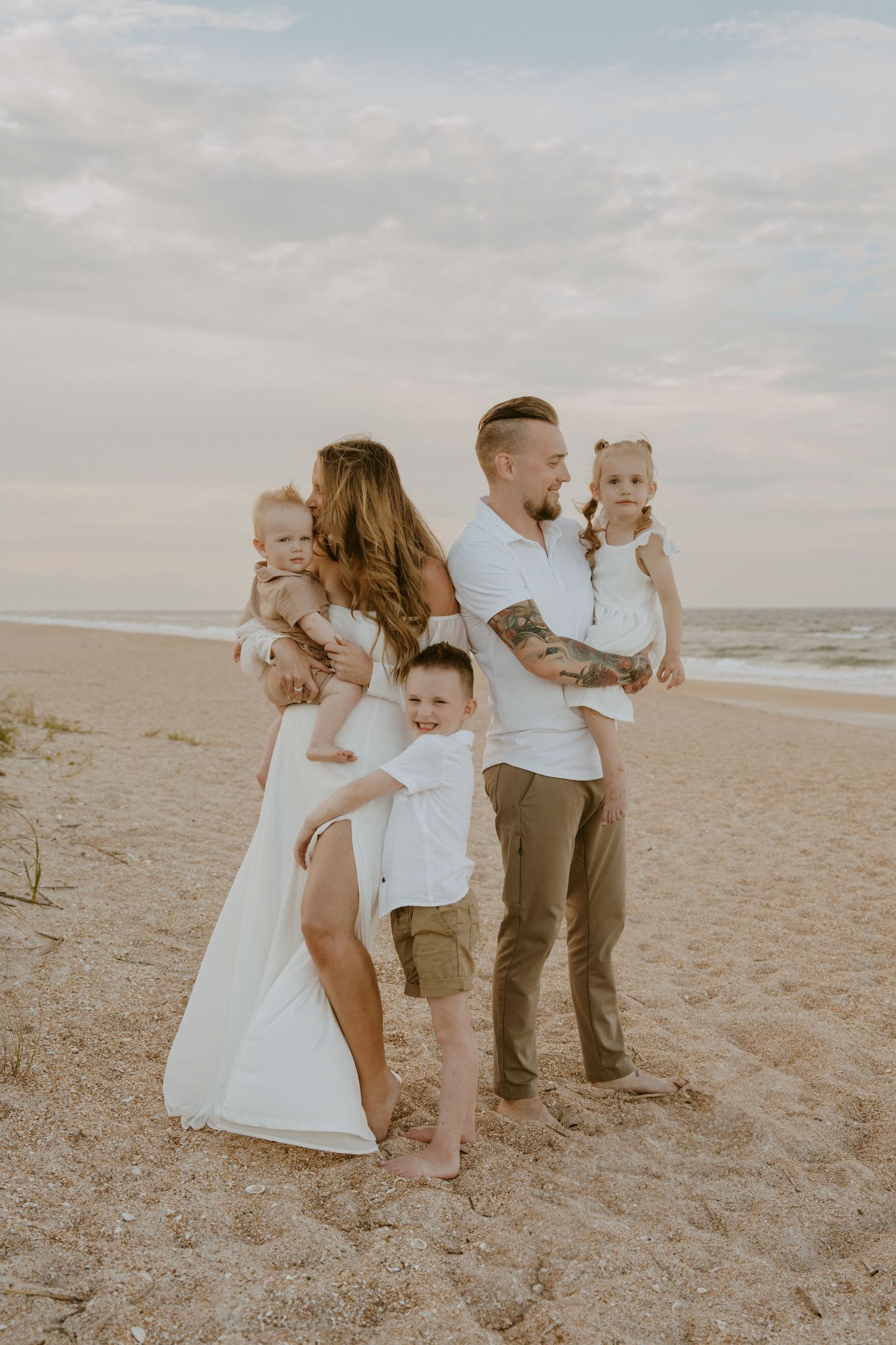 A family shares tender moments together on a sandy beach during a cloudy day photoshoot.