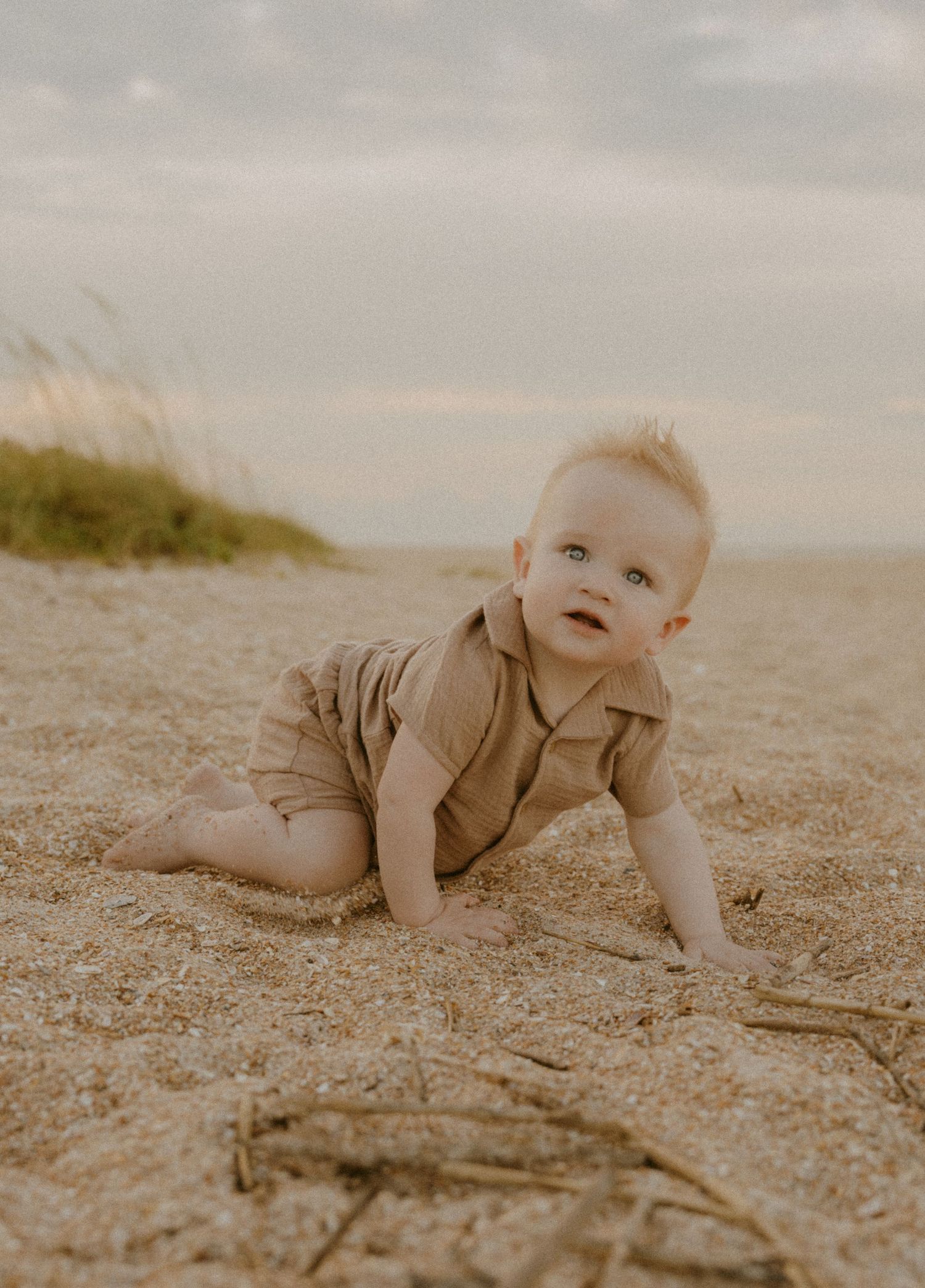 A baby crawls on sandy ground in a sepia-toned photo series showing movement across five sequential frames.
