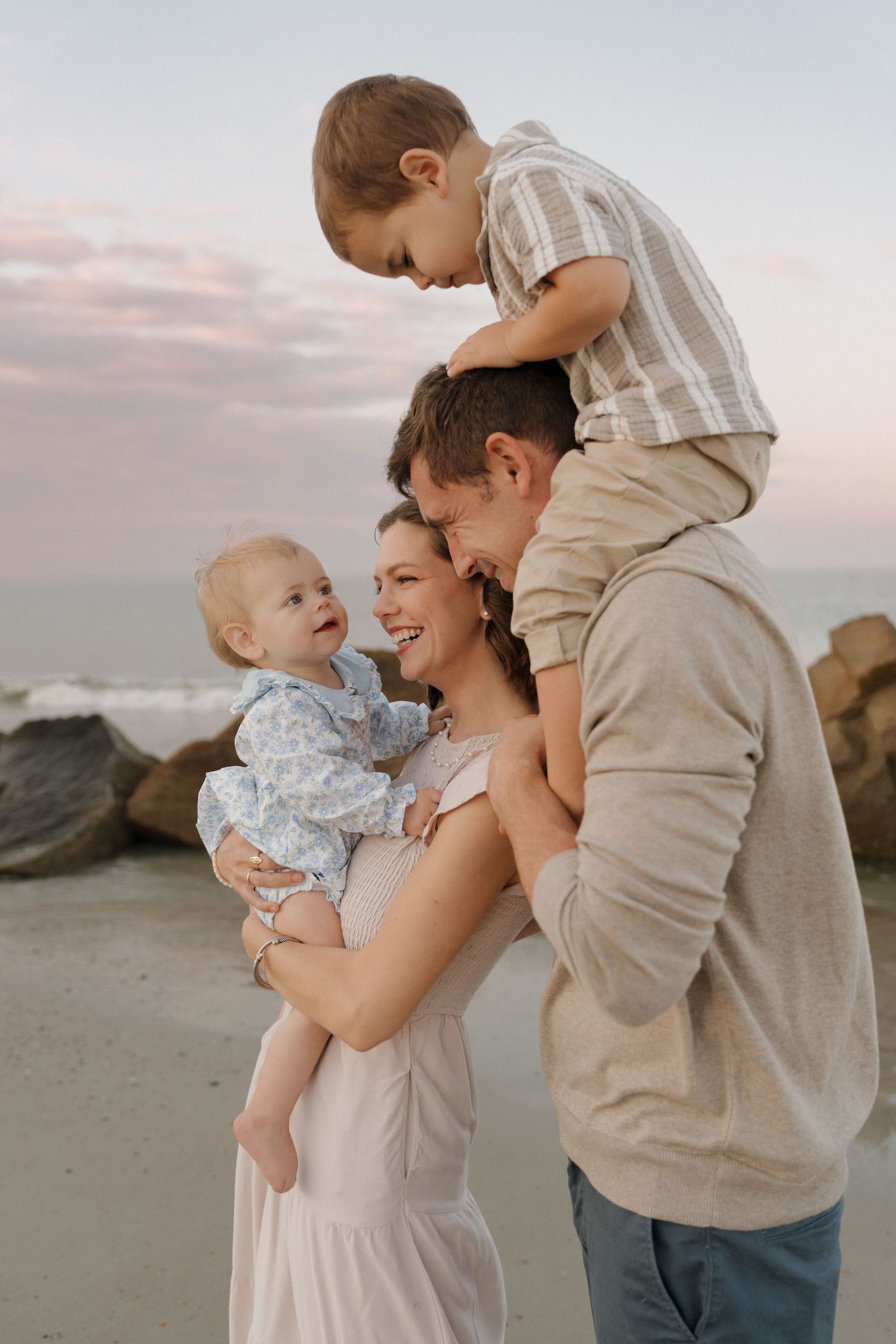 A family shares a tender moment together on a rocky beach at sunset.