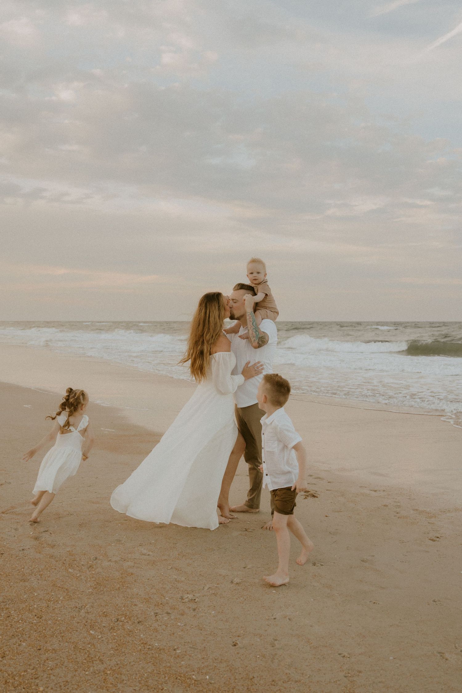 A family plays together on a sandy beach at sunset with waves rolling in the background.