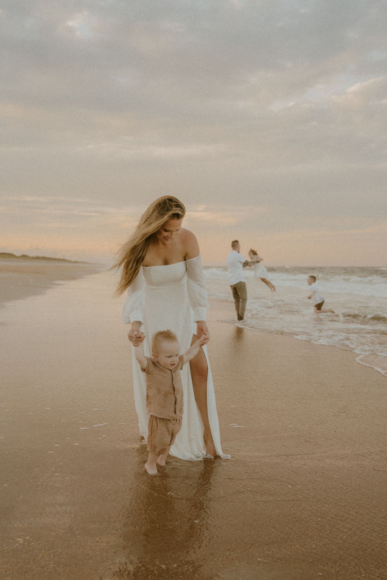 Family walking together on a misty beach at sunset with waves crashing in the background.