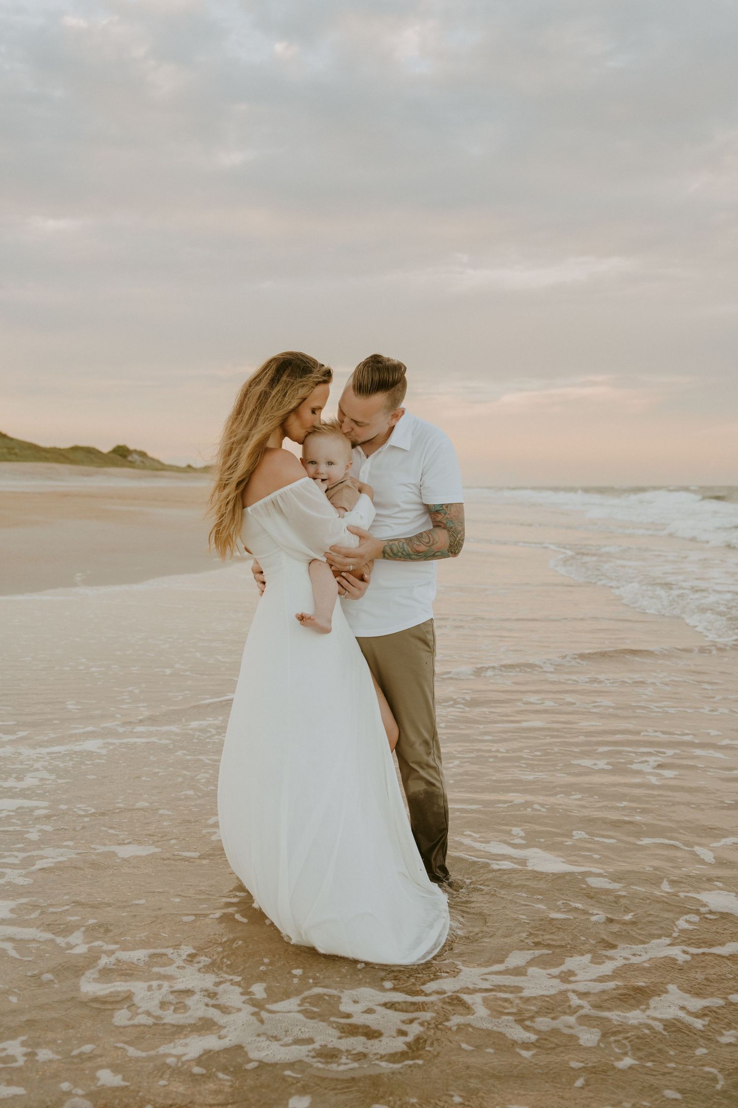 A couple embraces with their children on the beach as waves roll in during golden hour.