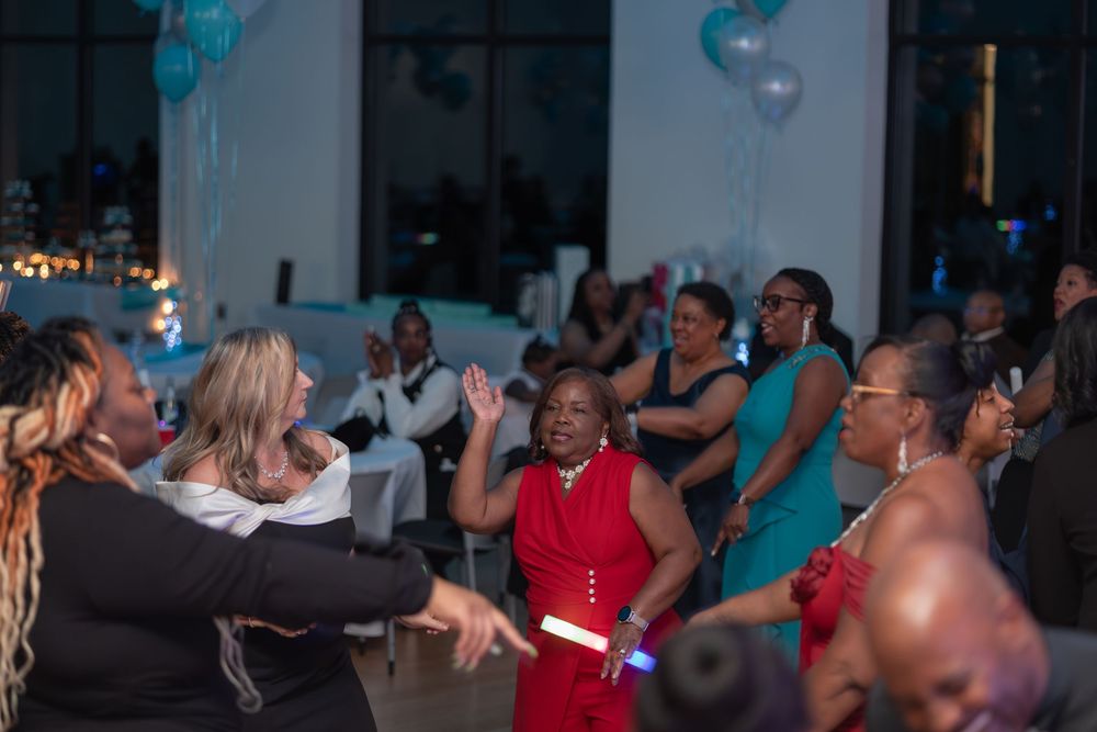 People dancing and celebrating at a lively indoor party with blue balloon decorations in the background.