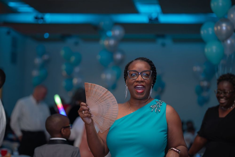 A guest in a turquoise dress holds a wooden fan while enjoying a celebration with blue lighting and balloons.