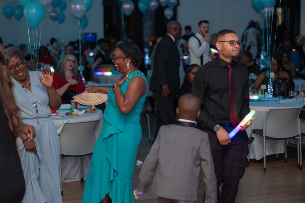 Guests enjoy a formal event with blue balloons decorating the venue as people mingle at round tables.