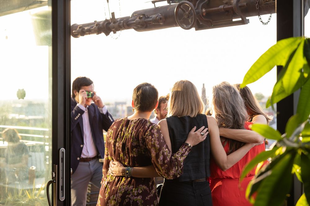 Group of elegantly dressed guests socializing on a rooftop terrace at a sunset event.