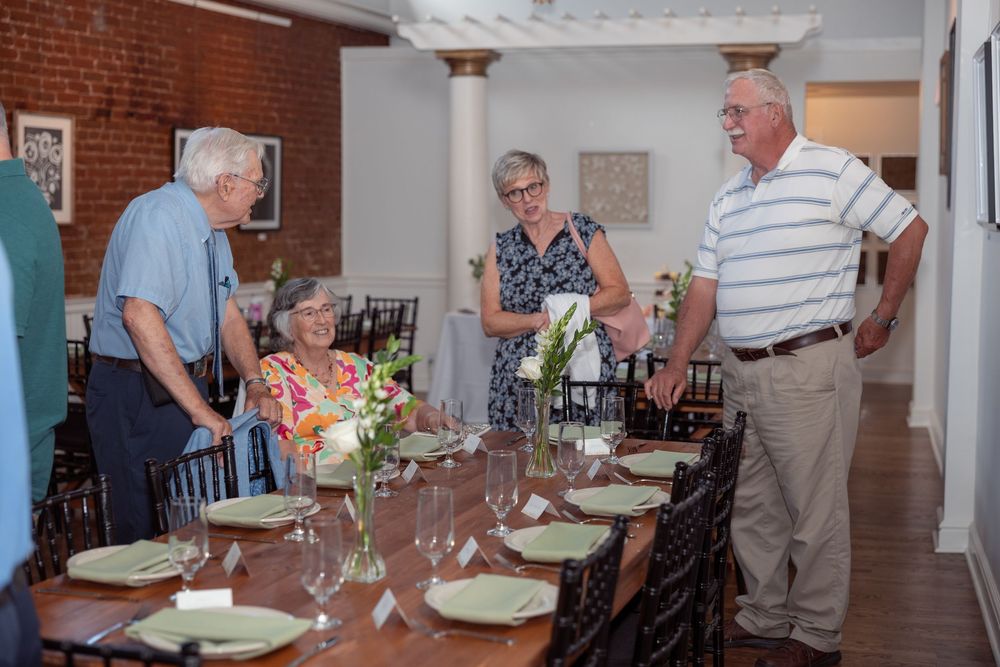 People gathered around tables at a social event in an indoor dining space with white walls and brick accents.