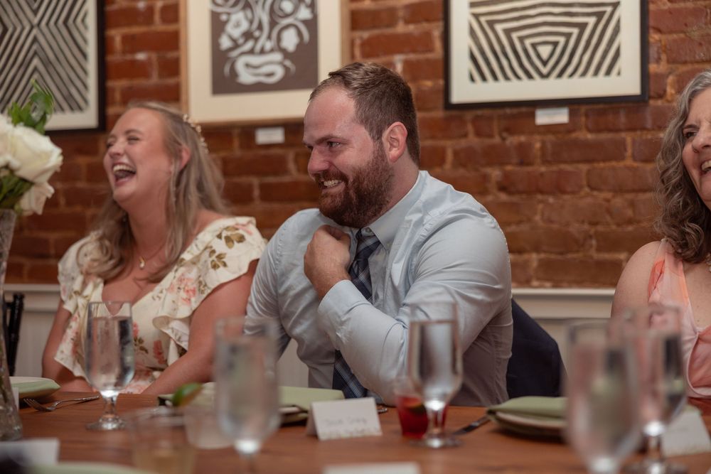 A group of people laughing and enjoying dinner together at a restaurant with exposed brick walls and artwork.