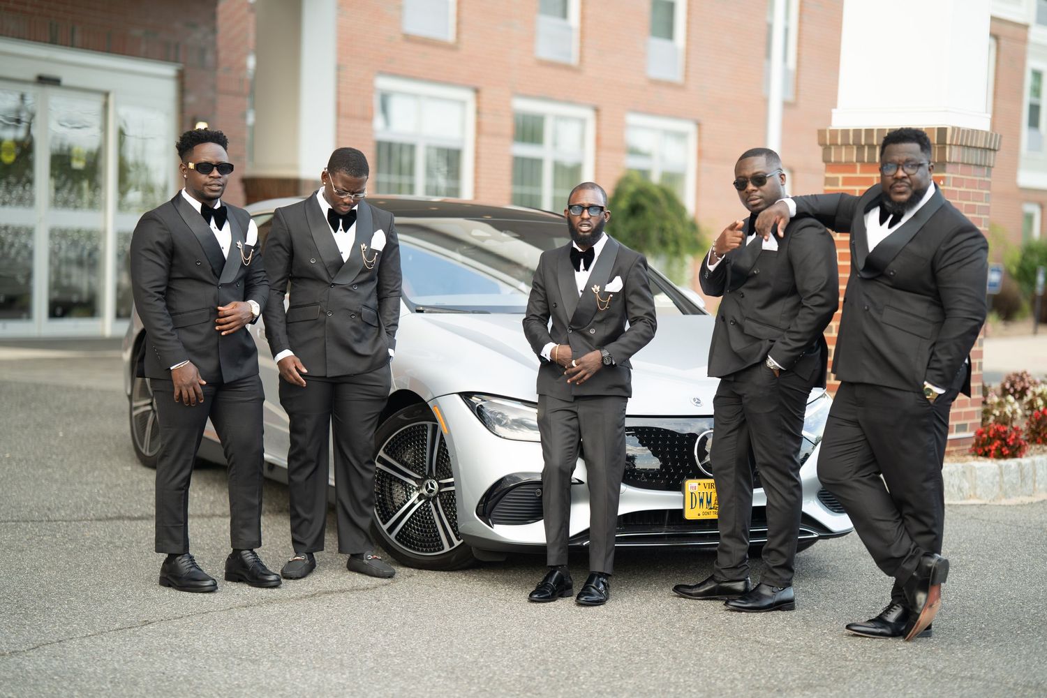 A row of people in formal black attire sitting on a curb showing off their colorful socks and dress shoes.