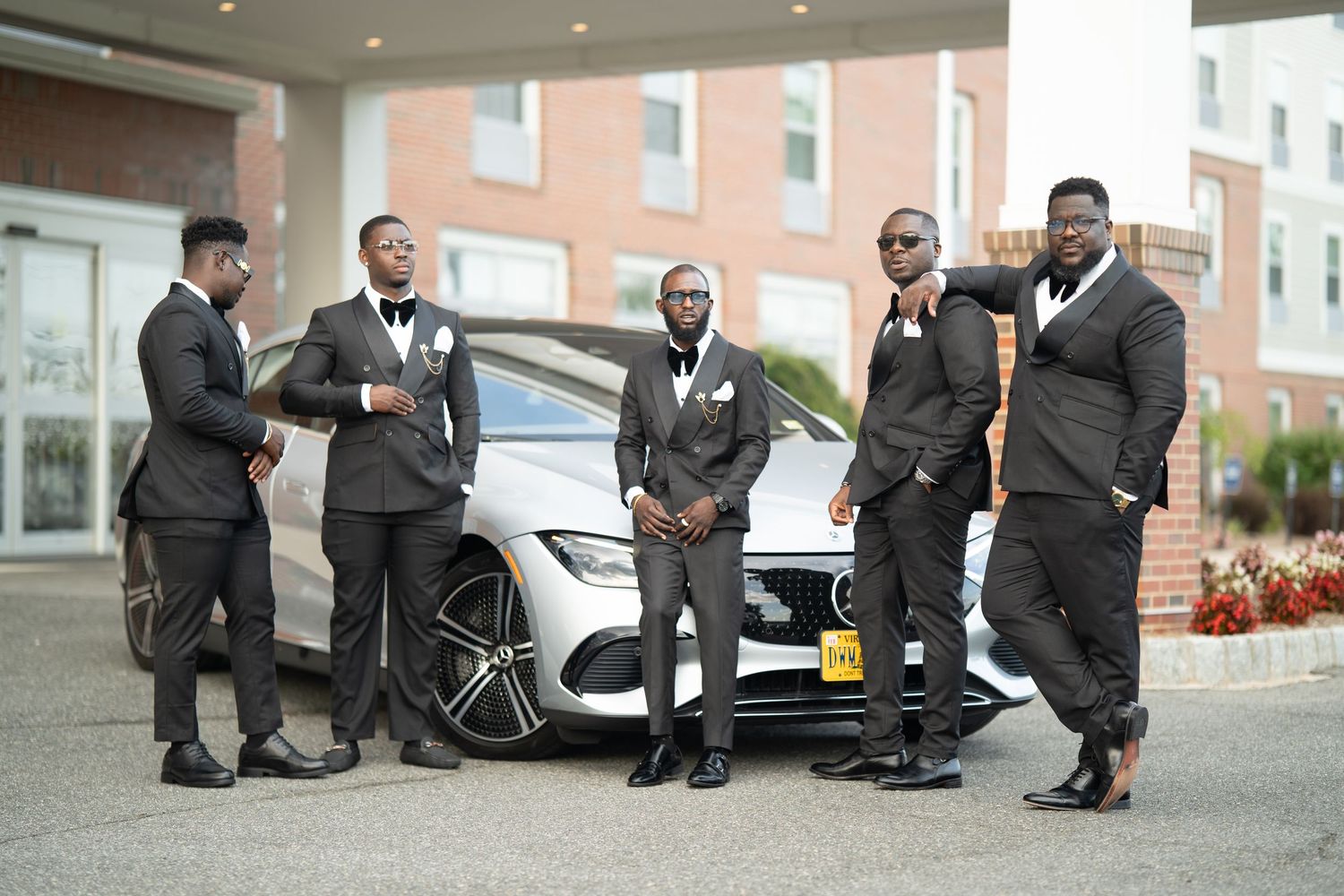 Groomsmen in black suits kneel to adjust their dress socks and shoes in a candid wedding photo lineup.
