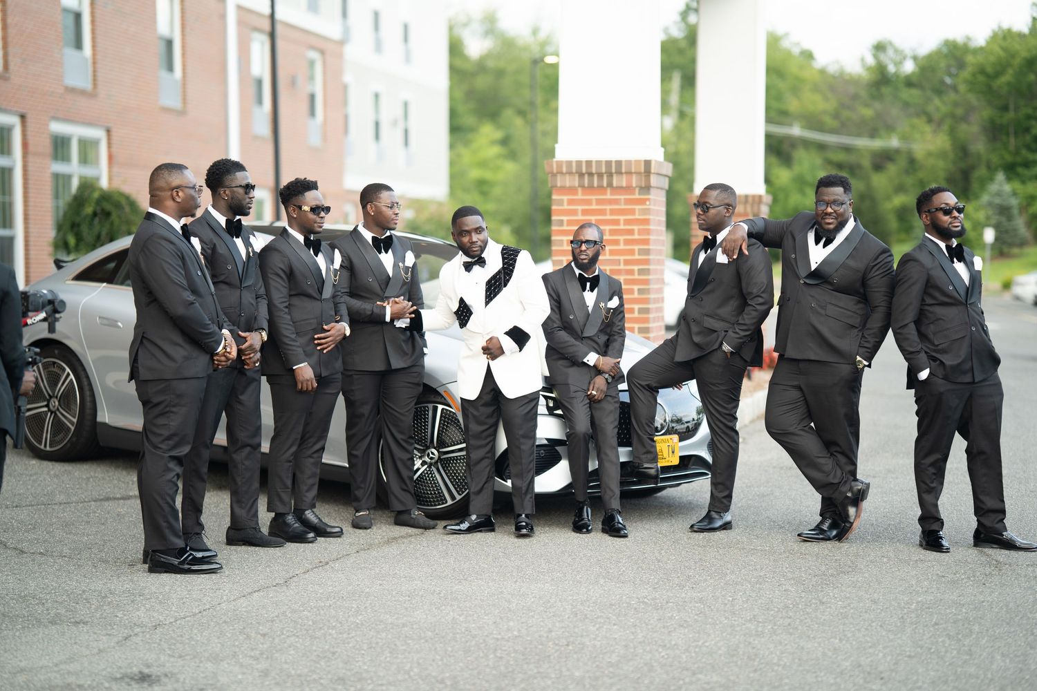 A group of people wearing black formal suits and ties gather together for a wedding party photo session outdoors.