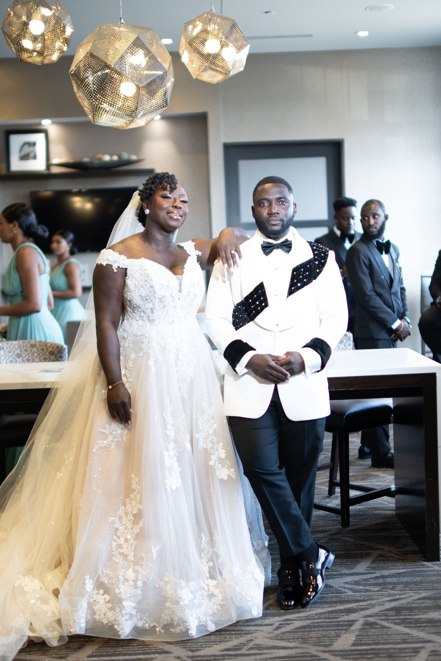 Wedding party dances and celebrates in an elegant reception venue with modern pendant lighting.