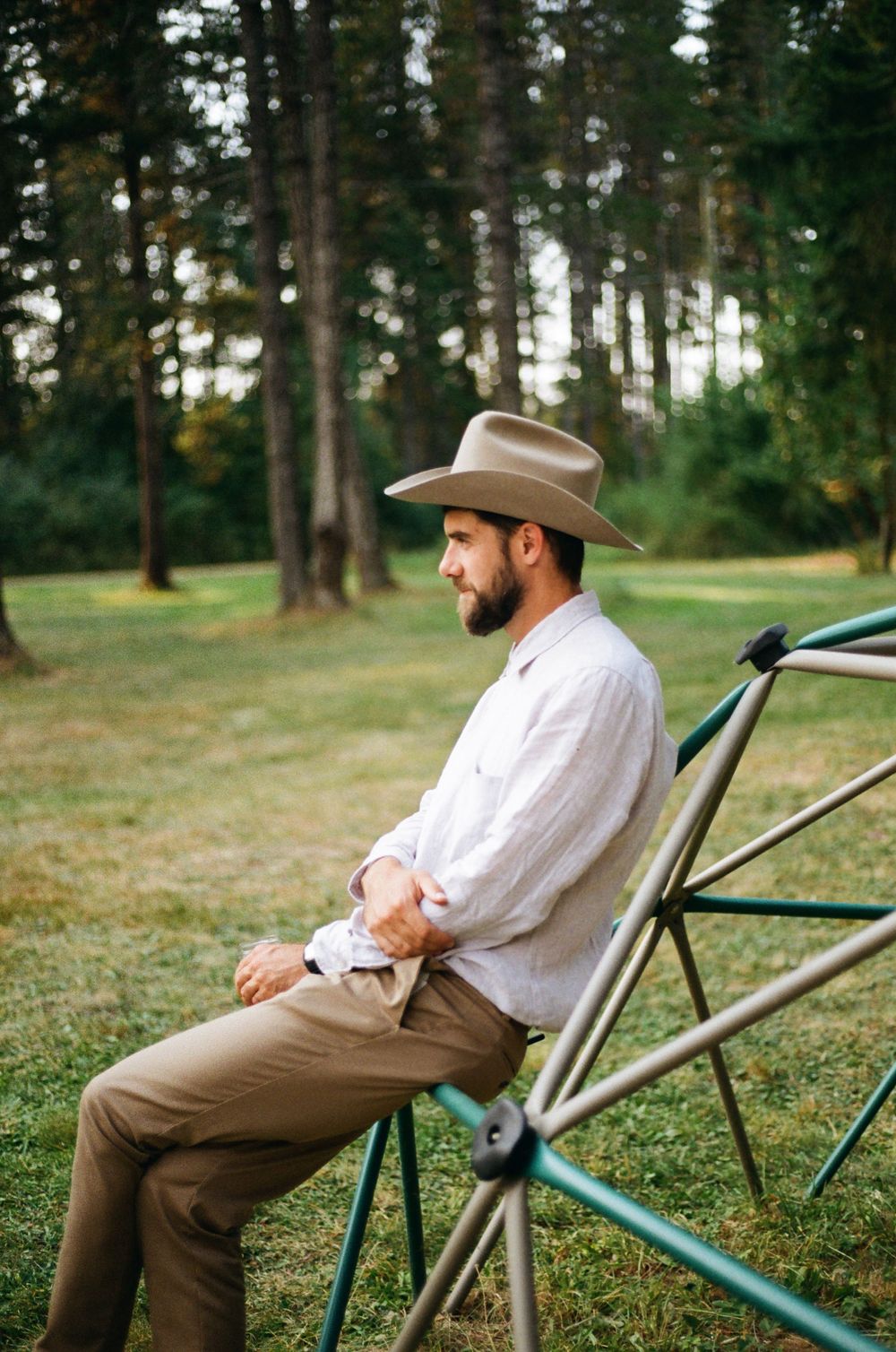 Person in casual attire and cowboy hat relaxing in a camping chair on a grassy hill.