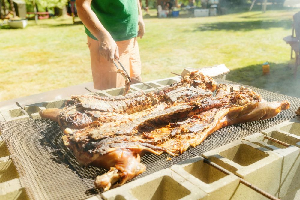 Large cuts of meat cooking on an outdoor barbecue grill.
