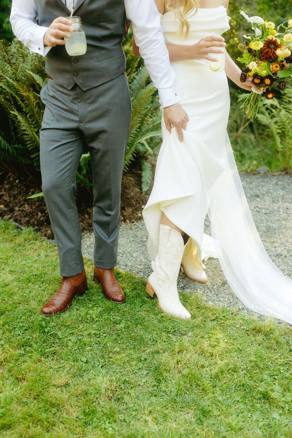 Close-up of formal wedding attire showing brown leather shoes and white dress hem on grass.