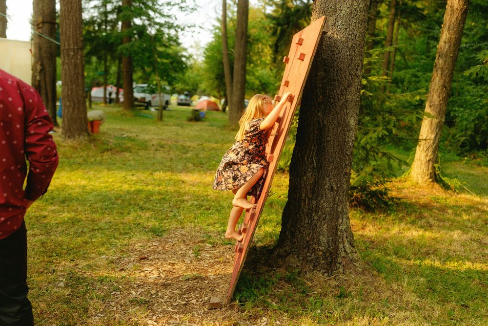 A decorative wooden carving leans against a tree trunk in a grassy outdoor setting.