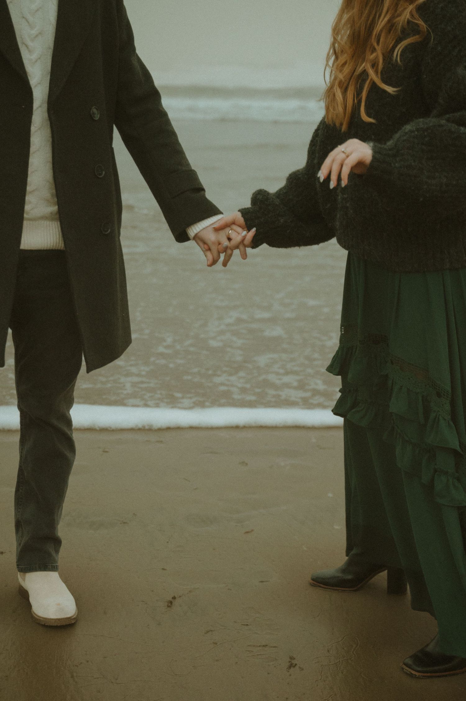 A group of people wearing formal black attire stand together on a sandy beach during overcast weather.