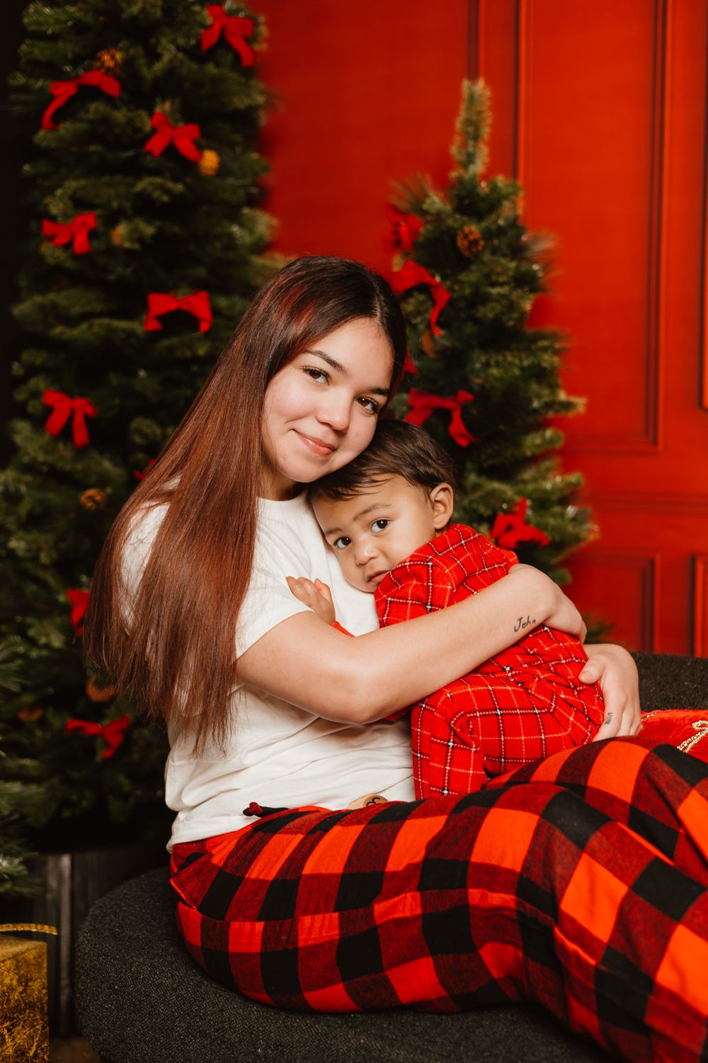 A tender holiday moment shared on a couch with red and black buffalo plaid decor and Christmas trees in the background.