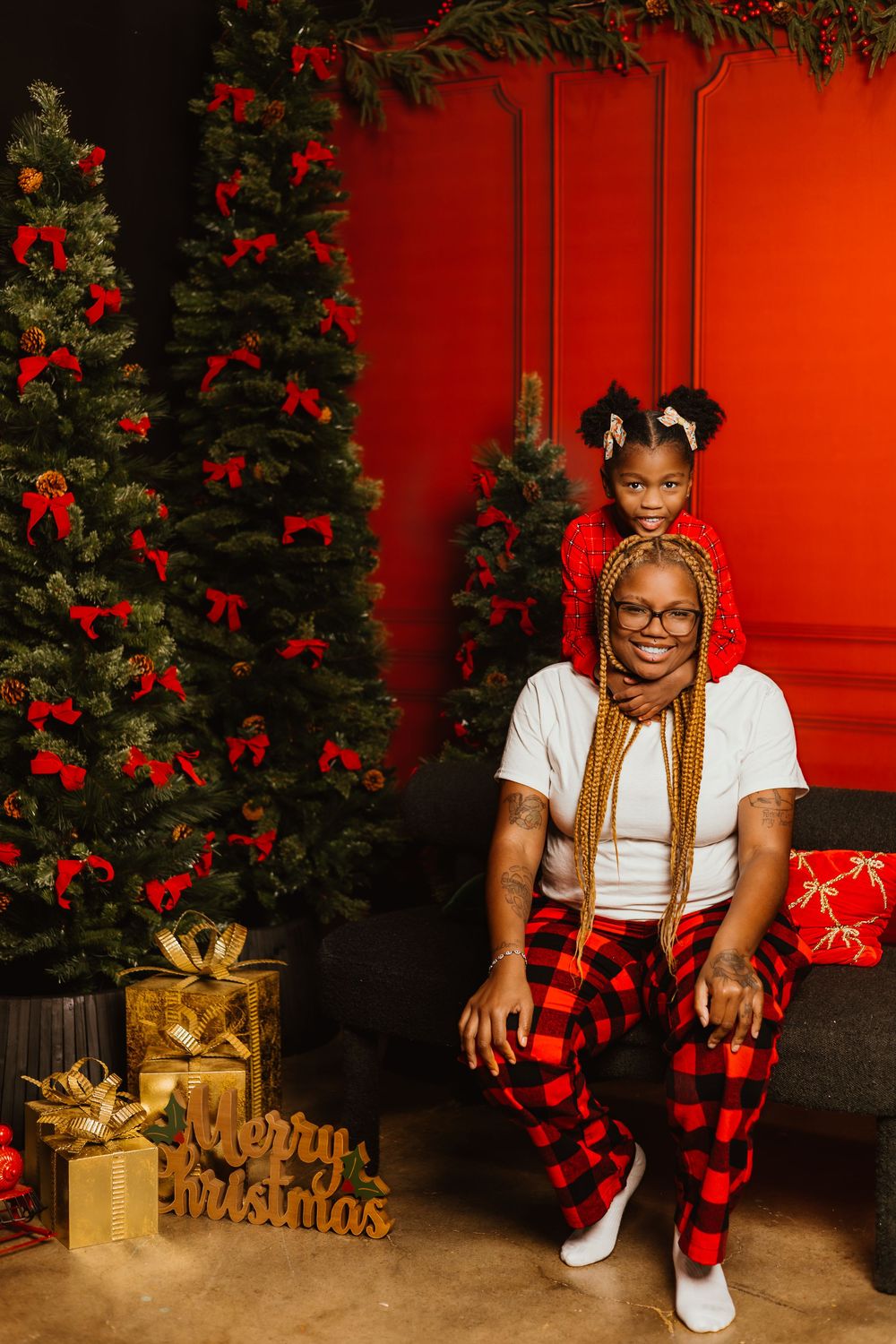 Holiday photo session with Christmas decorations featuring red door backdrop, gold presents, and buffalo plaid accents.