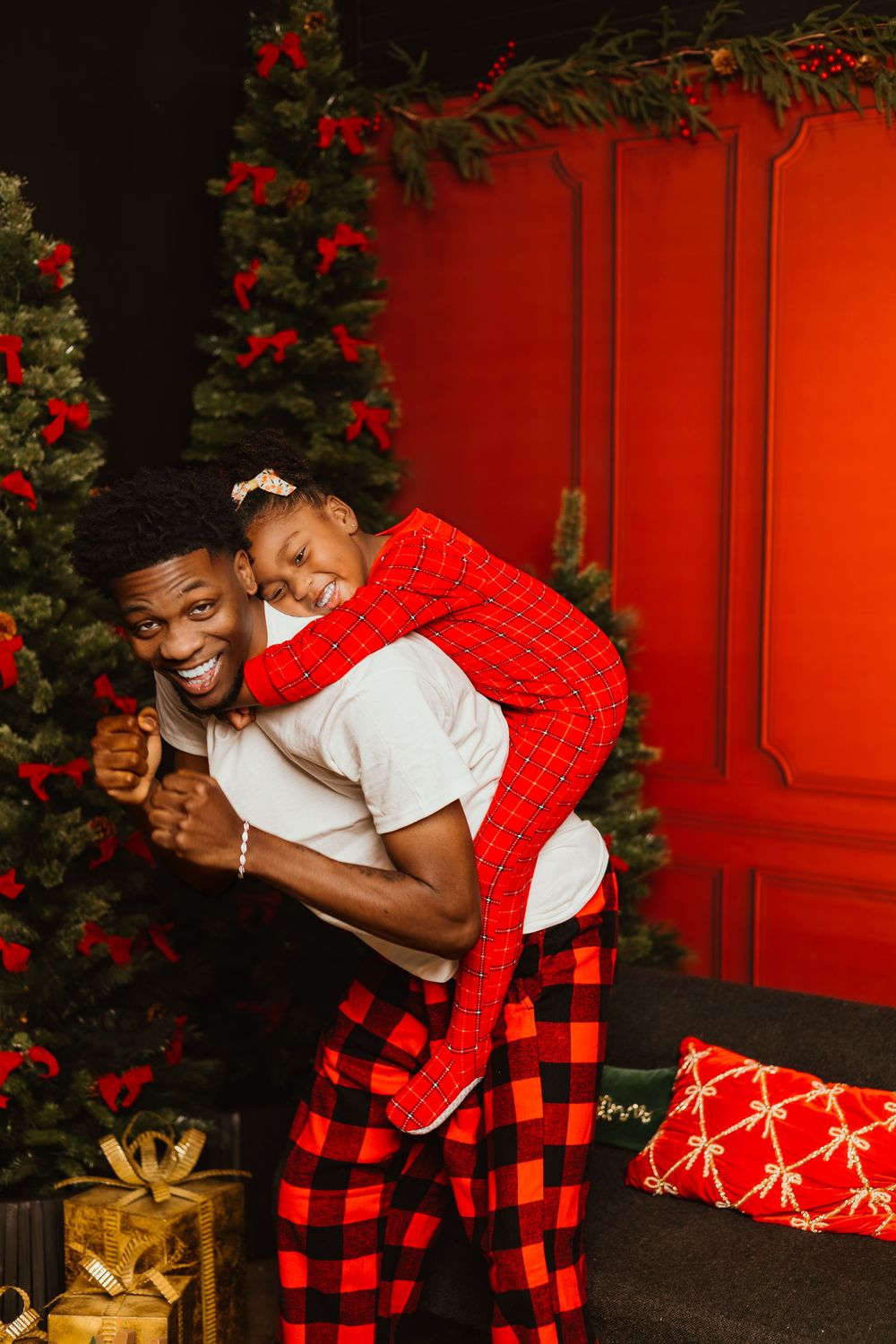 Festive holiday scene with decorated Christmas tree, red door, buffalo plaid pajamas, and wrapped presents on the floor.