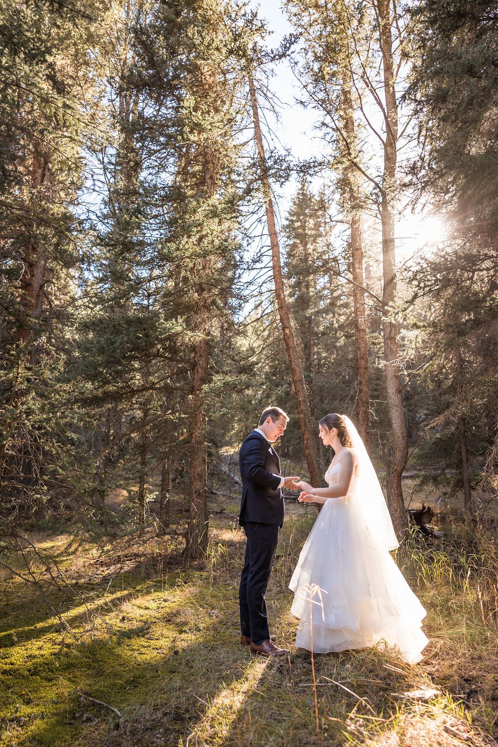 A couple shares an intimate moment in a sunlit forest clearing during their wedding ceremony.