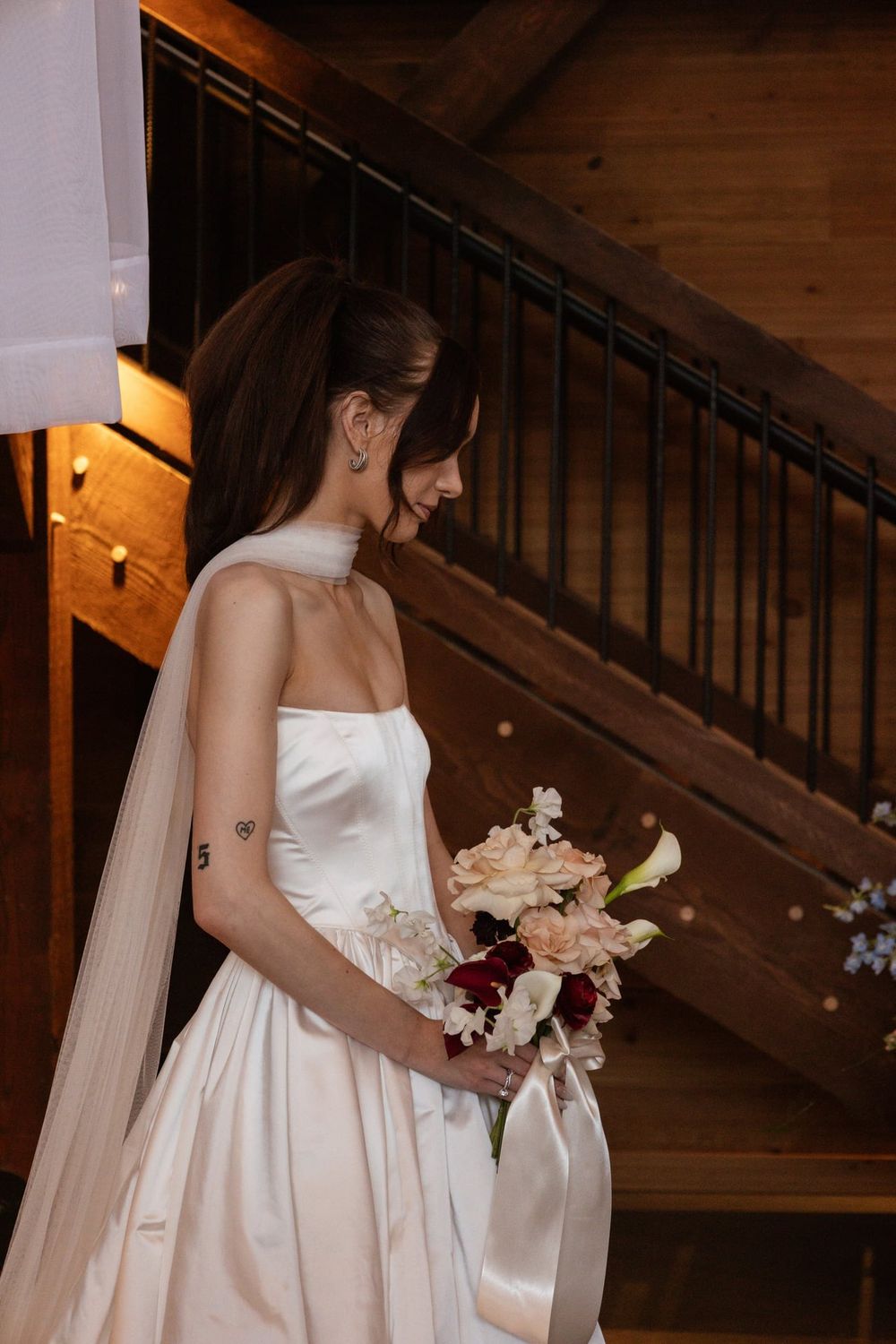 Elegant bride in white satin dress holding bouquet in rustic wooden venue.