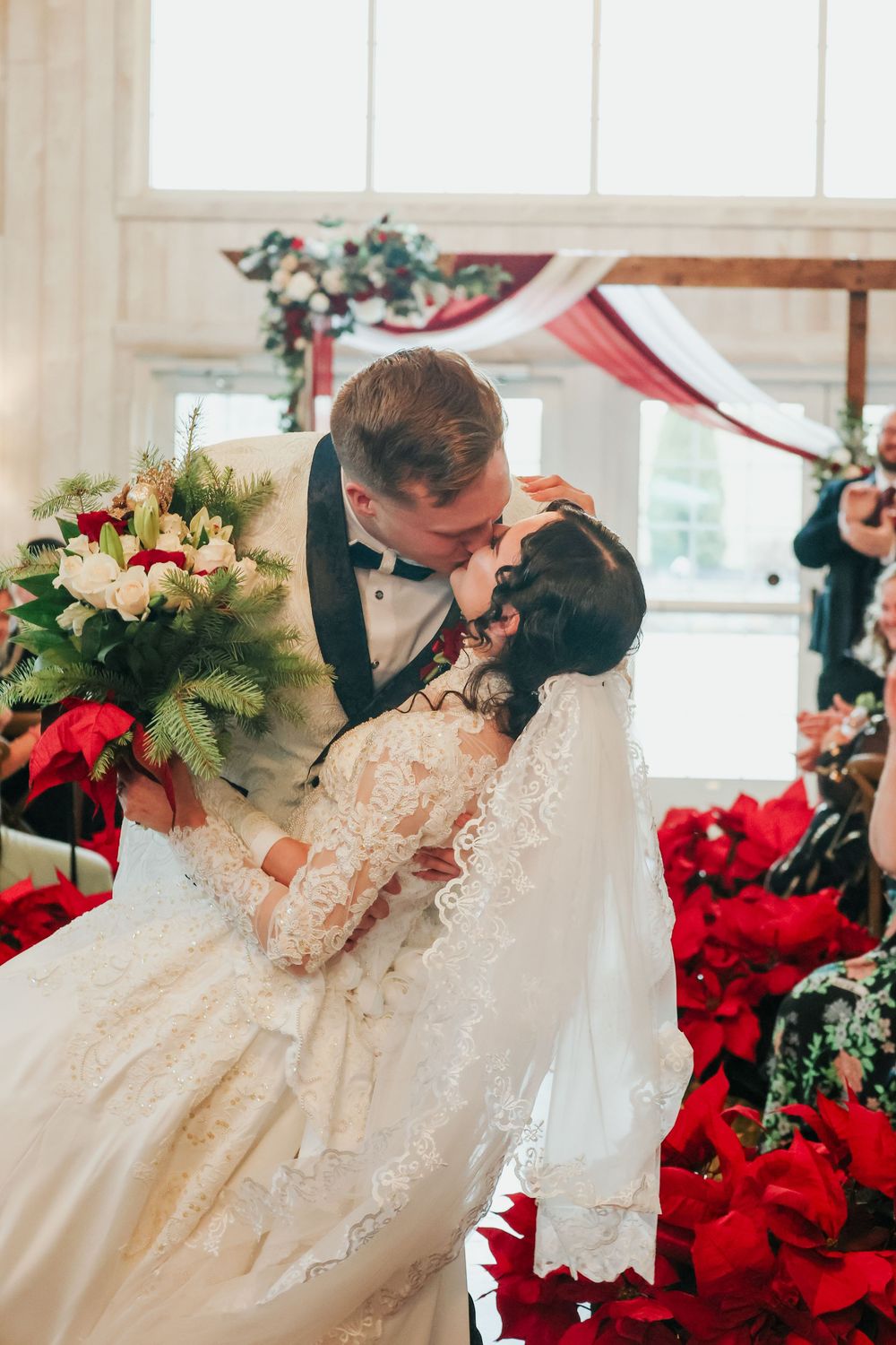 Wedding dress details with red poinsettias and greenery in a bright indoor setting.