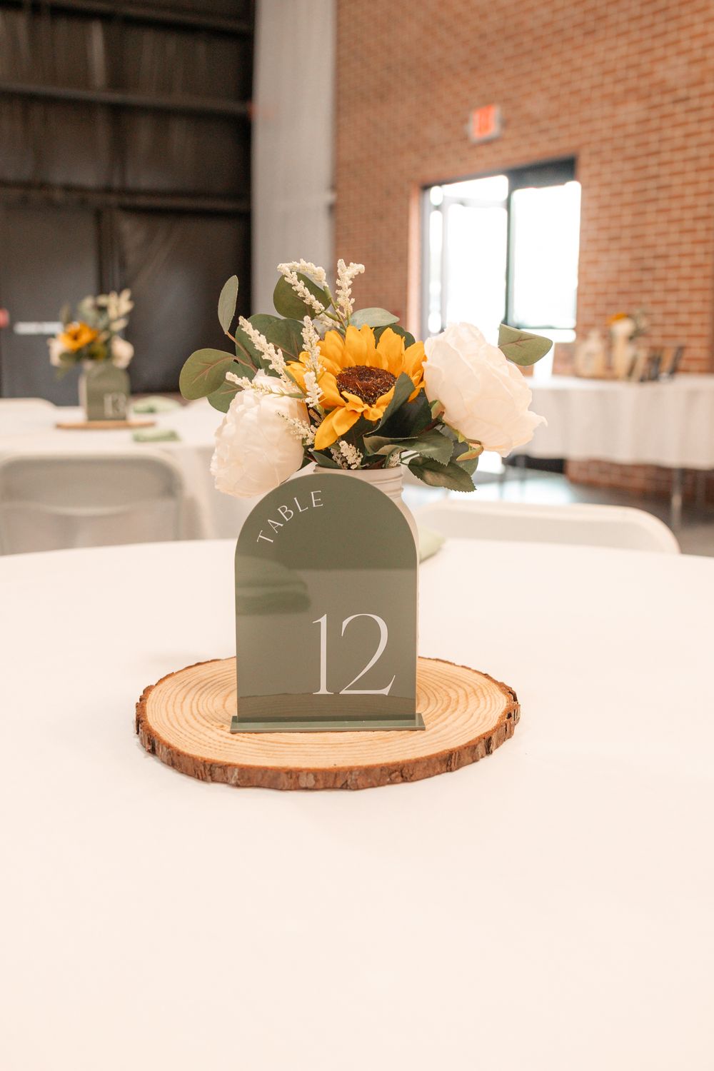 Wedding table 12 centerpiece with sunflower, white roses, eucalyptus on wood slice with sage green arch sign.