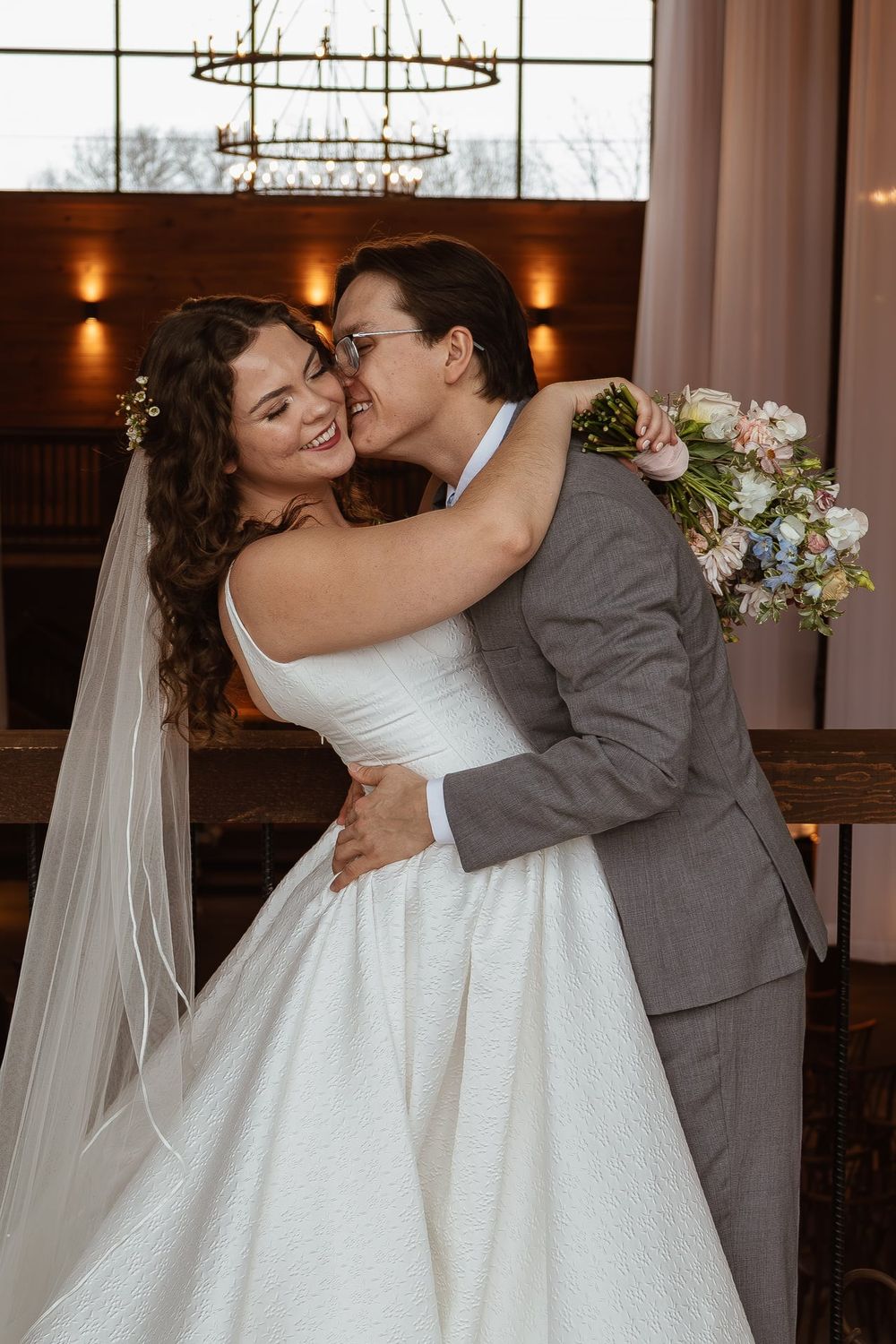 Romantic moment captured between newlyweds in venue with chandeliers and natural light.