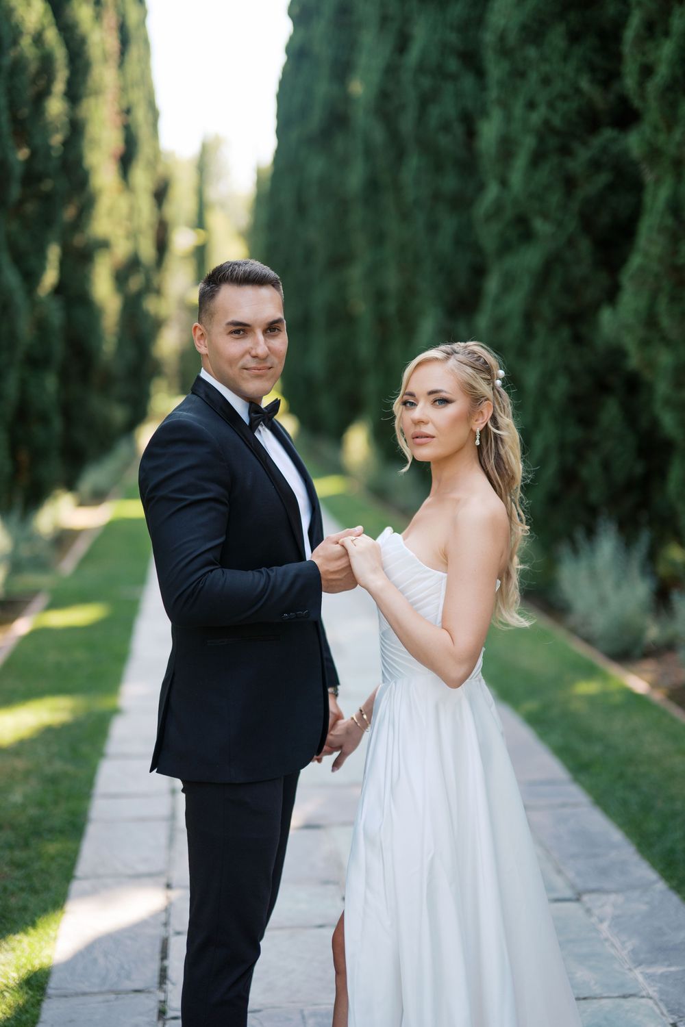 A romantic wedding couple dances together on a cypress tree-lined path in soft natural lighting.
