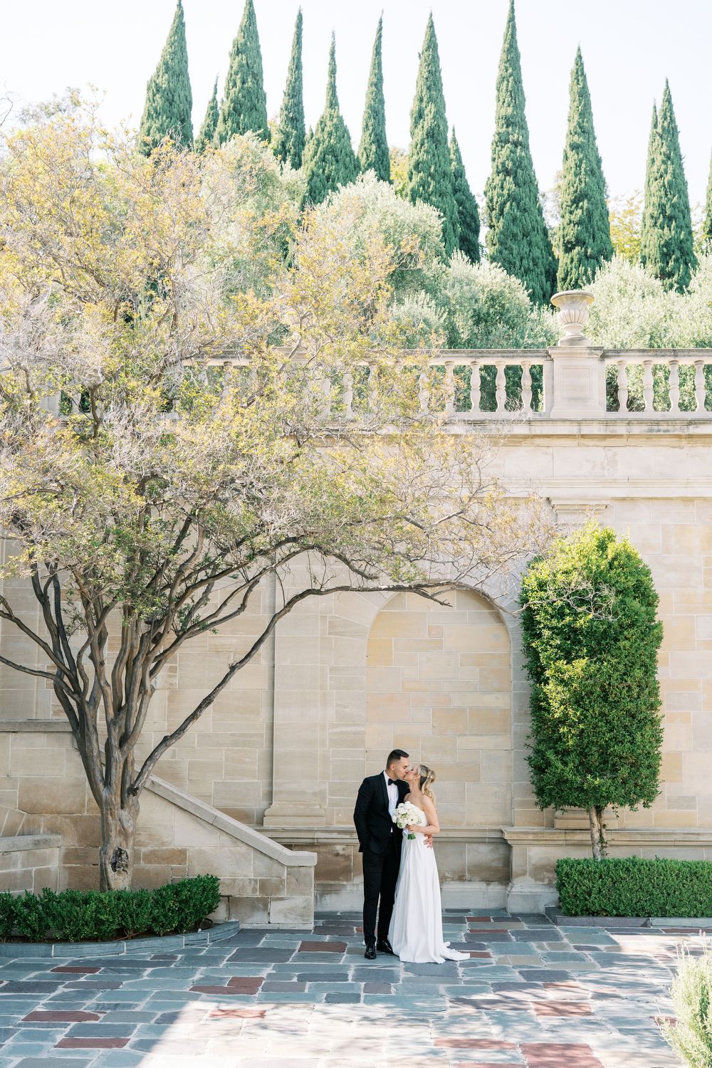 A serene courtyard setting with stone walls, flowering trees, and paved walkways creates an elegant backdrop.