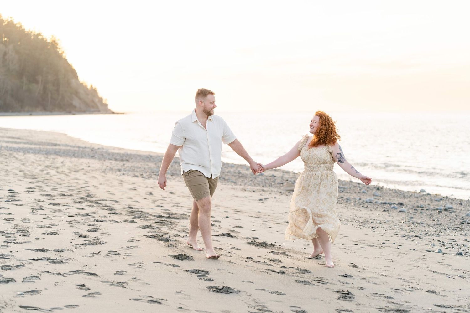 Couple walking hand in hand along a scenic beach at sunset during a romantic photoshoot.