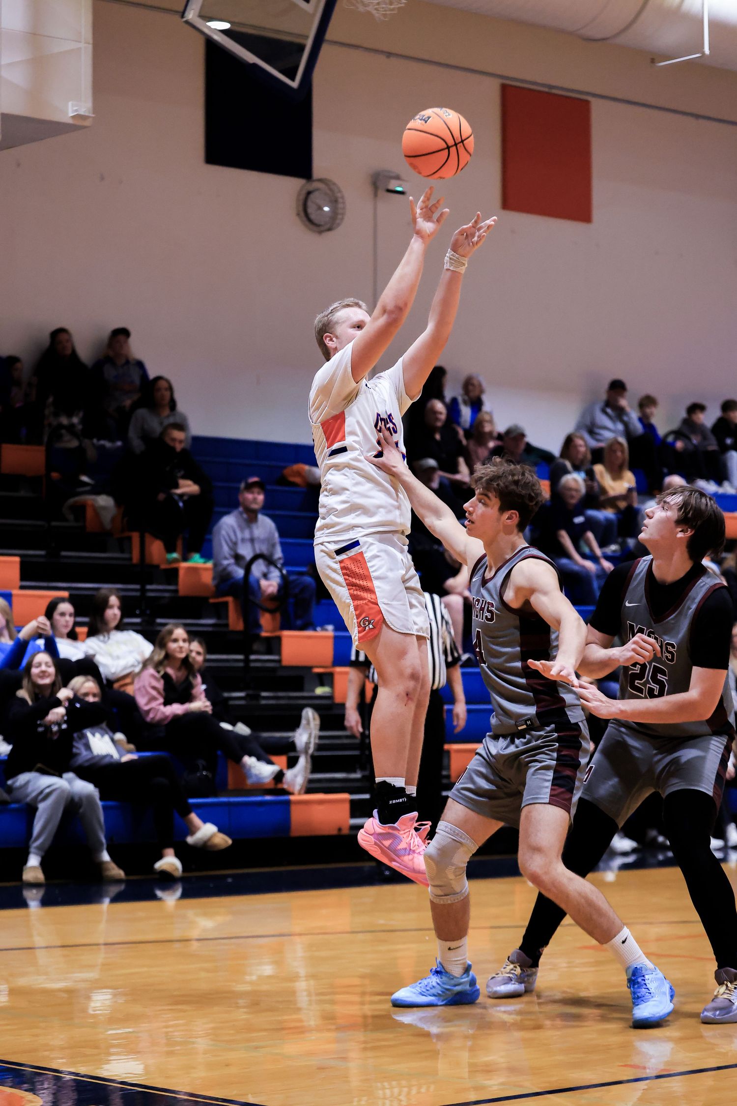 Basketball players compete for possession during an intense indoor game with spectators watching.