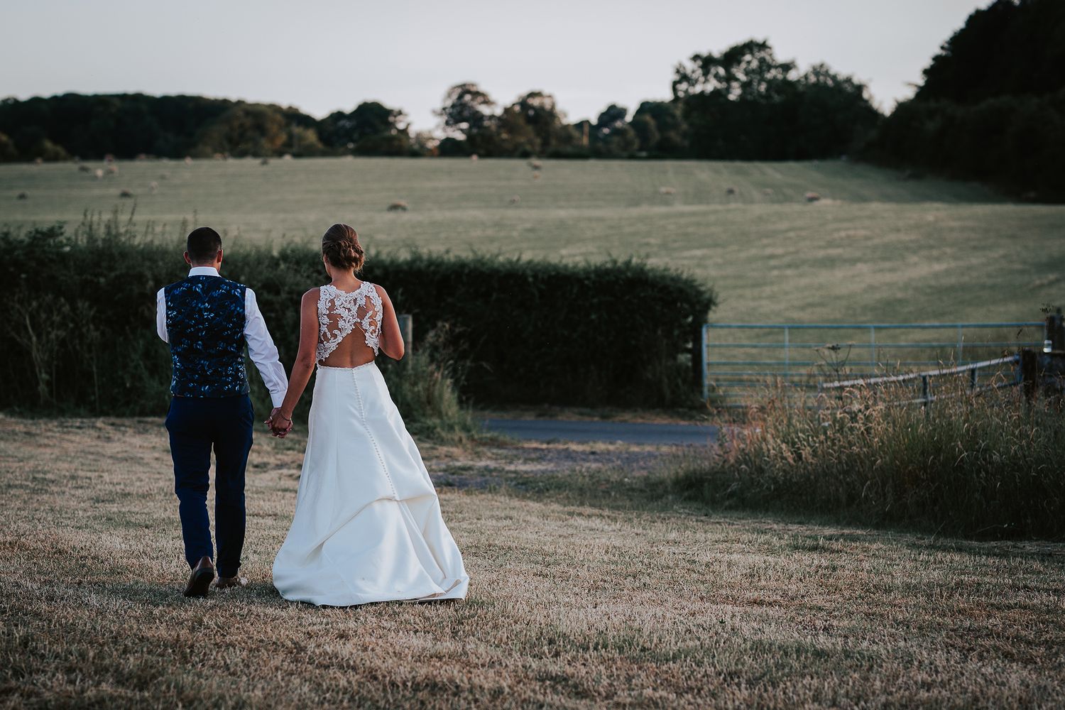 Wedding couple walking through a serene countryside field at dusk.