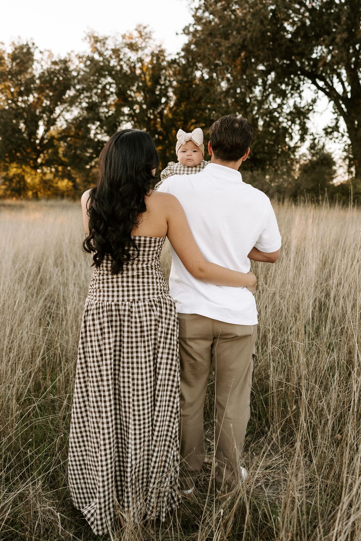 A couple embraces while walking through a golden field of tall grass at sunset, shown in a series of candid shots.