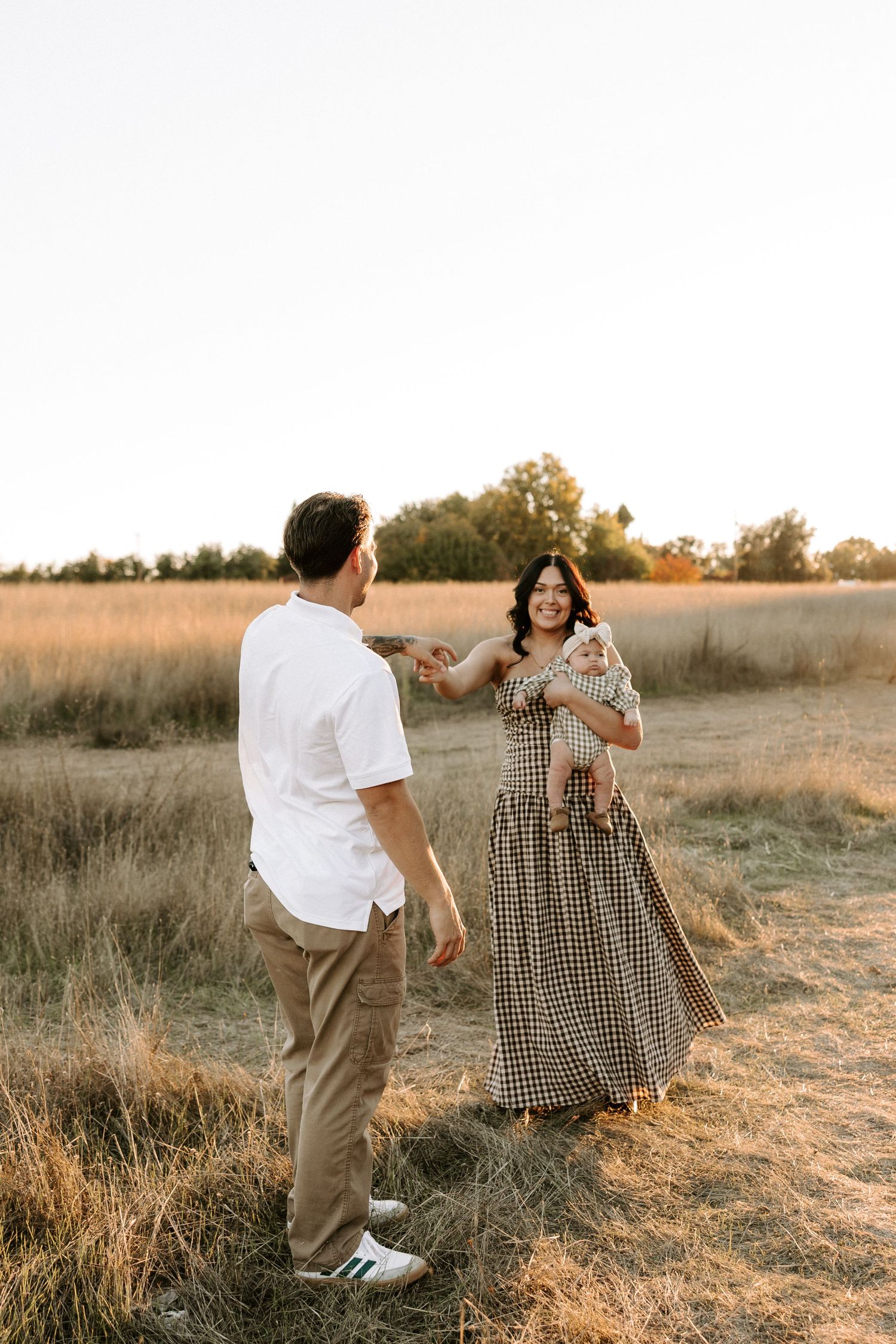 A couple in vintage-inspired outfits dance together in a golden sunlit field during sunset.