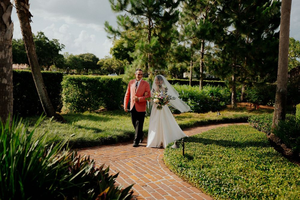 A rustic brick building with white trim and lush gardens creates an elegant outdoor wedding venue setting.