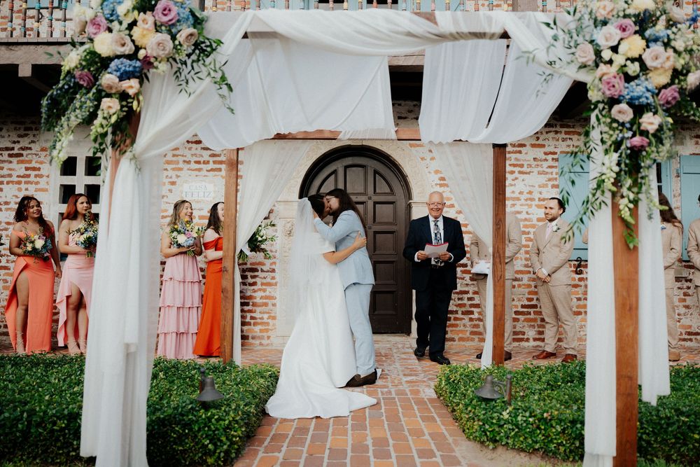 Elegant wedding ceremony setup with white columns, floral arrangements, and exposed brick walls at an outdoor venue.