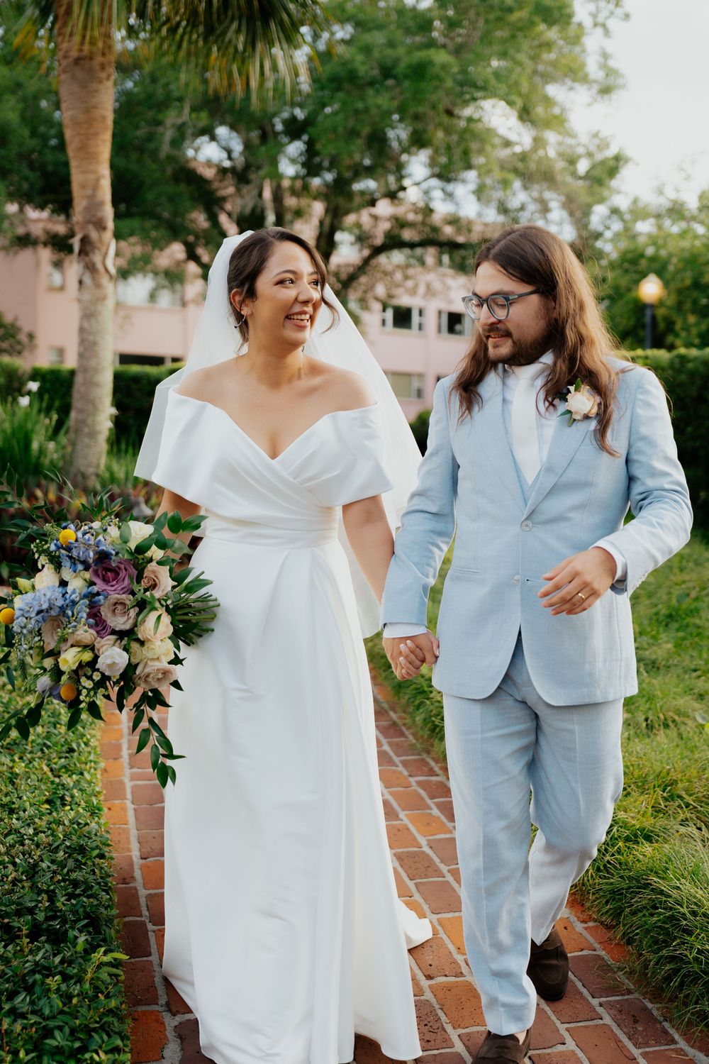 Wedding couple walking together on a brick path through a garden setting.