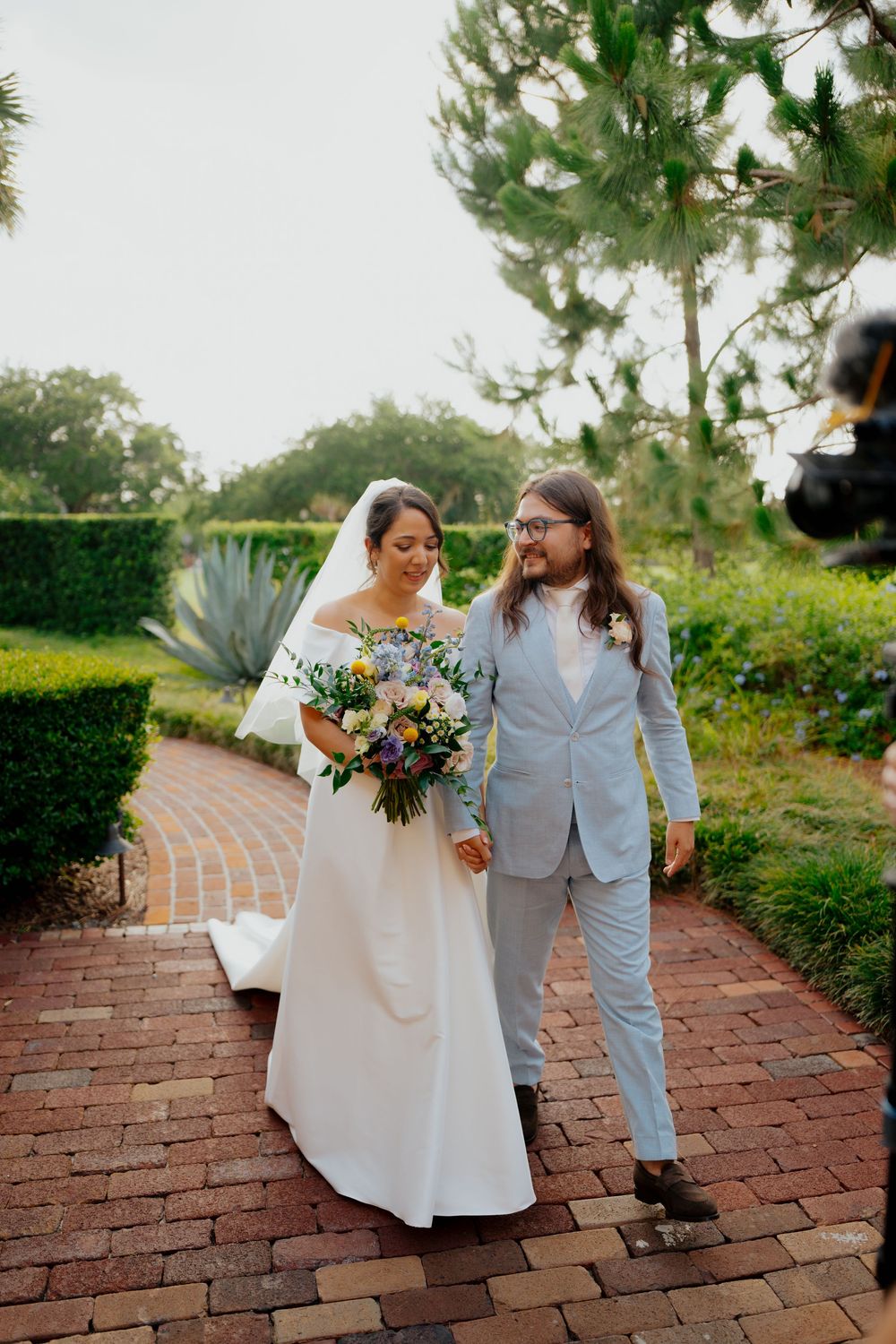 Couple sharing a joyful moment while walking along a garden brick pathway.