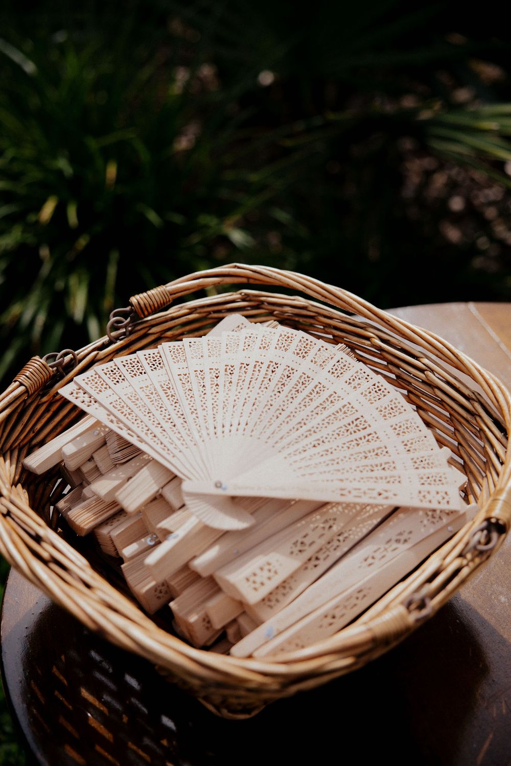 Decorative wooden folding fans arranged in a wicker basket for wedding guests or events.