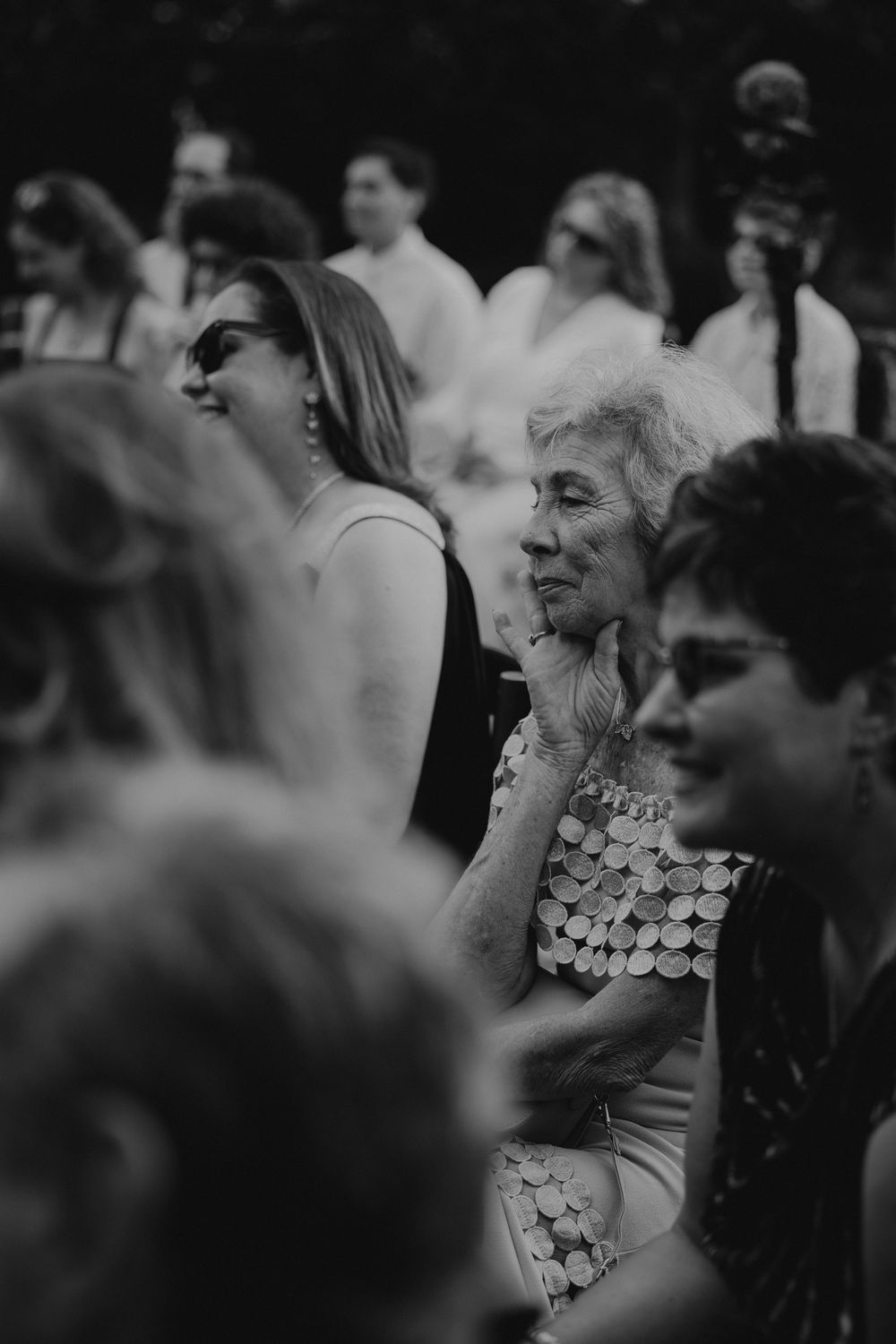 A black and white photo shows a crowd of wedding guests gathered at an outdoor celebration.